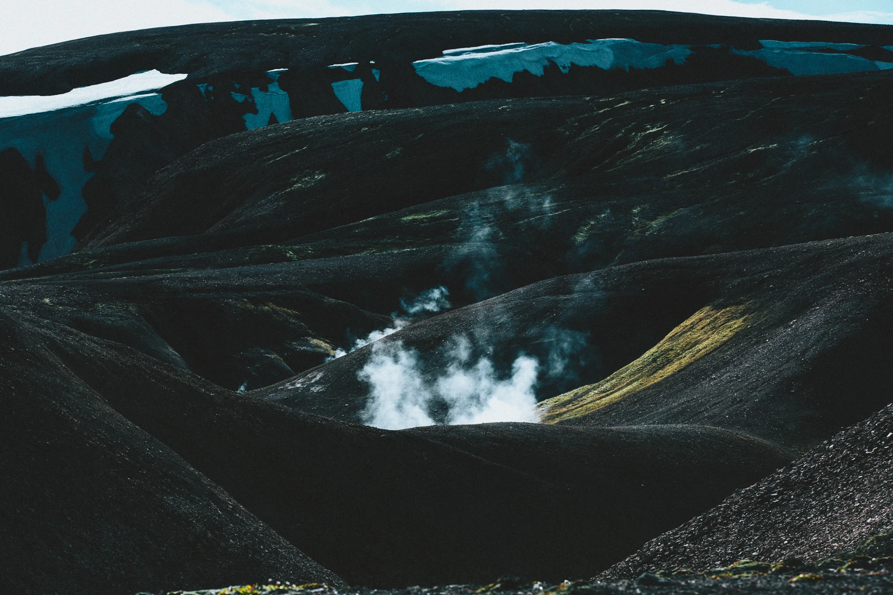 Steam venting from a fissure in black volcanic ground streaked with snow