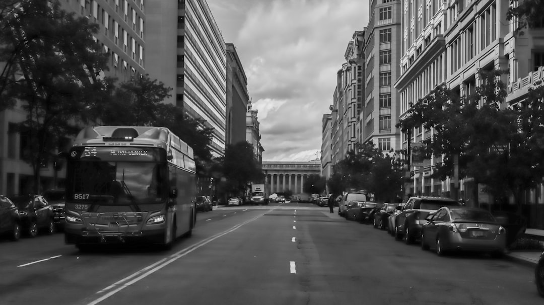 Bus traveling down a wide urban boulevard flanked by classical government buildings.