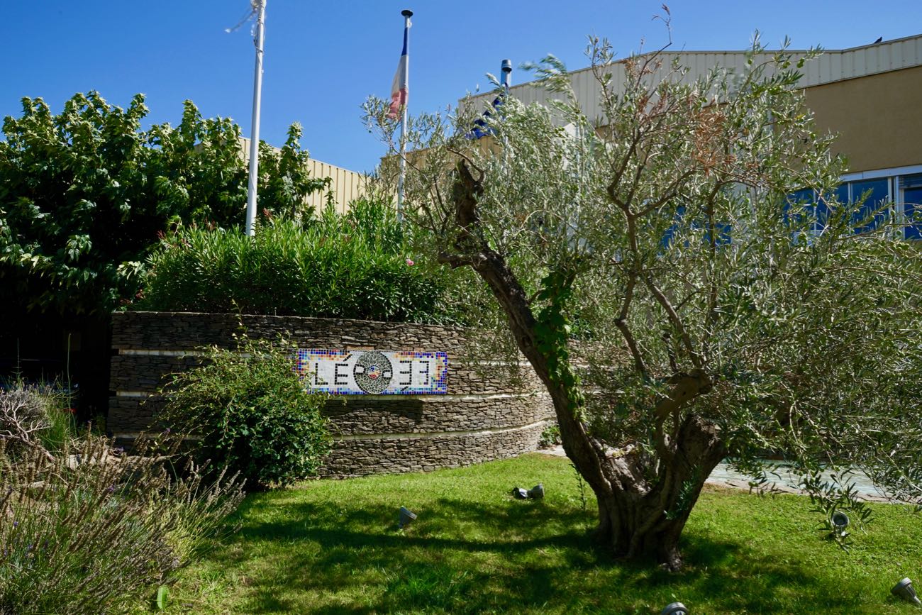 Un jardin avec un mur en pierre surélevé portant une mosaïque avec l’inscription “L’épopée”.