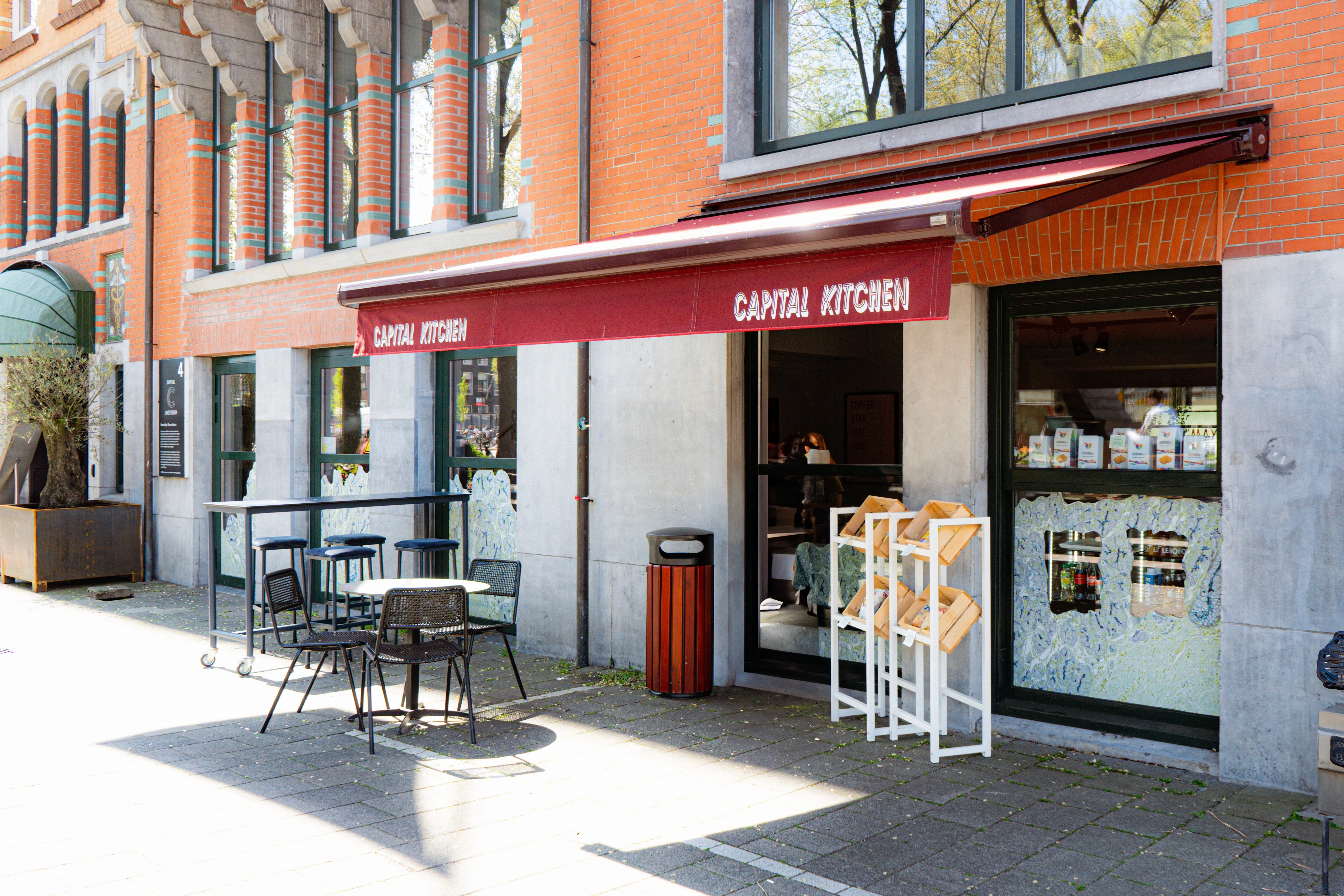 A storefront with a red awning, featuring large windows and a sidewalk sign, set against a colorful building.