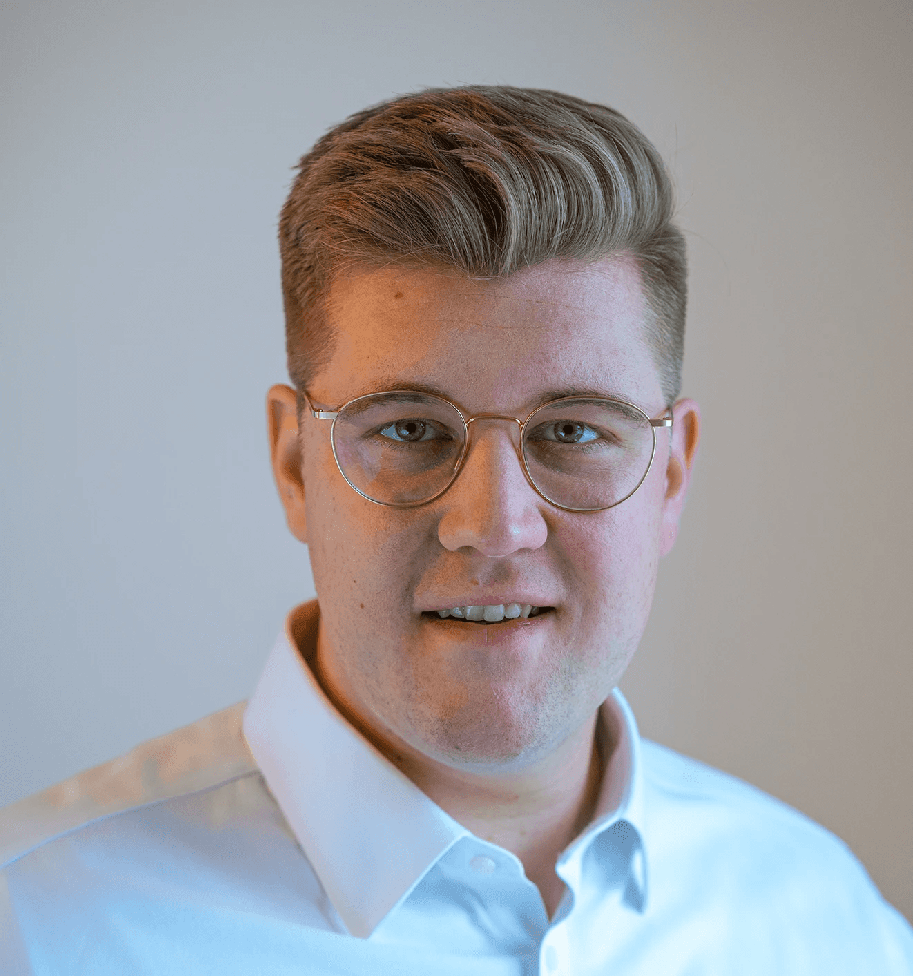 A young person with short, light-colored hair and glasses is looking directly at the camera.