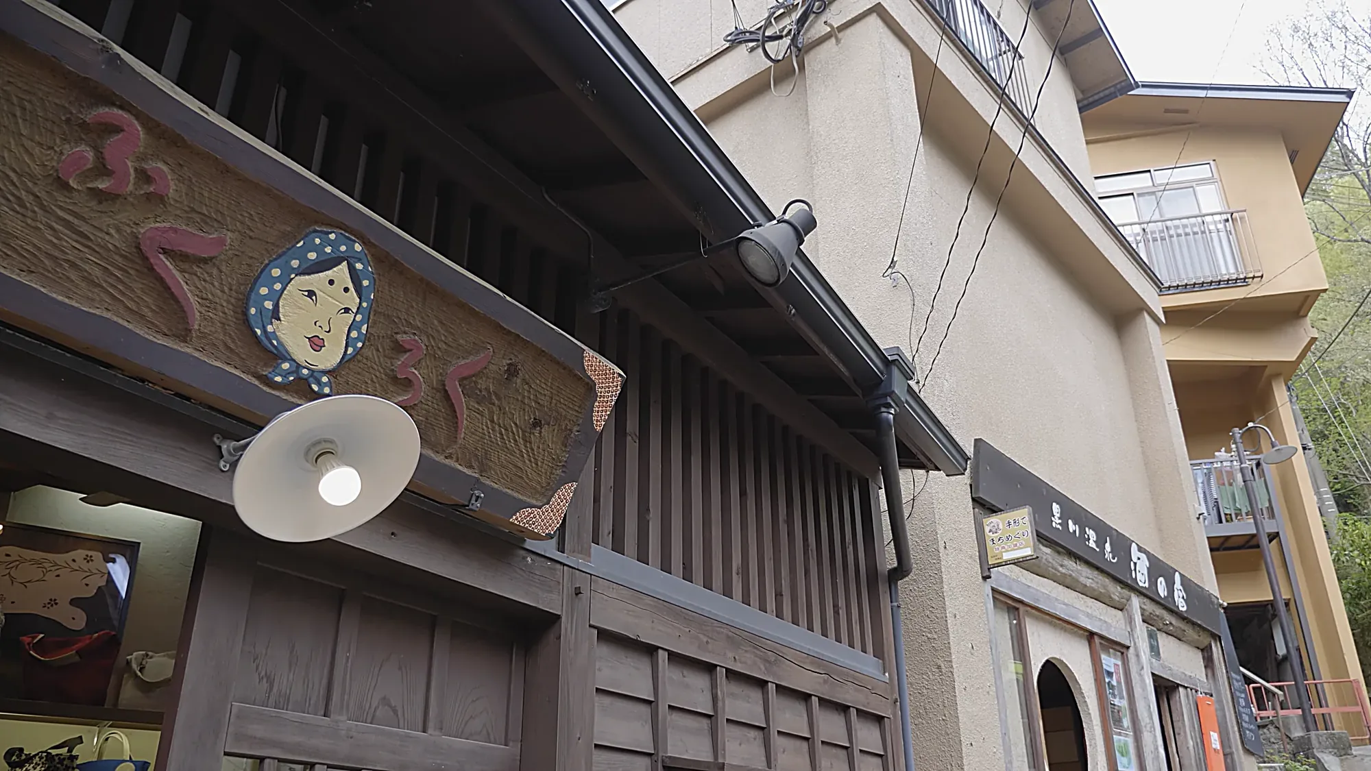A painted shopfront sign with a face motif on a timber facade at Kurokawa Onsen