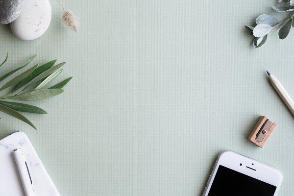 Minimal workspace flat lay with smartphone, pencil, notebook, and greenery on a neutral background.