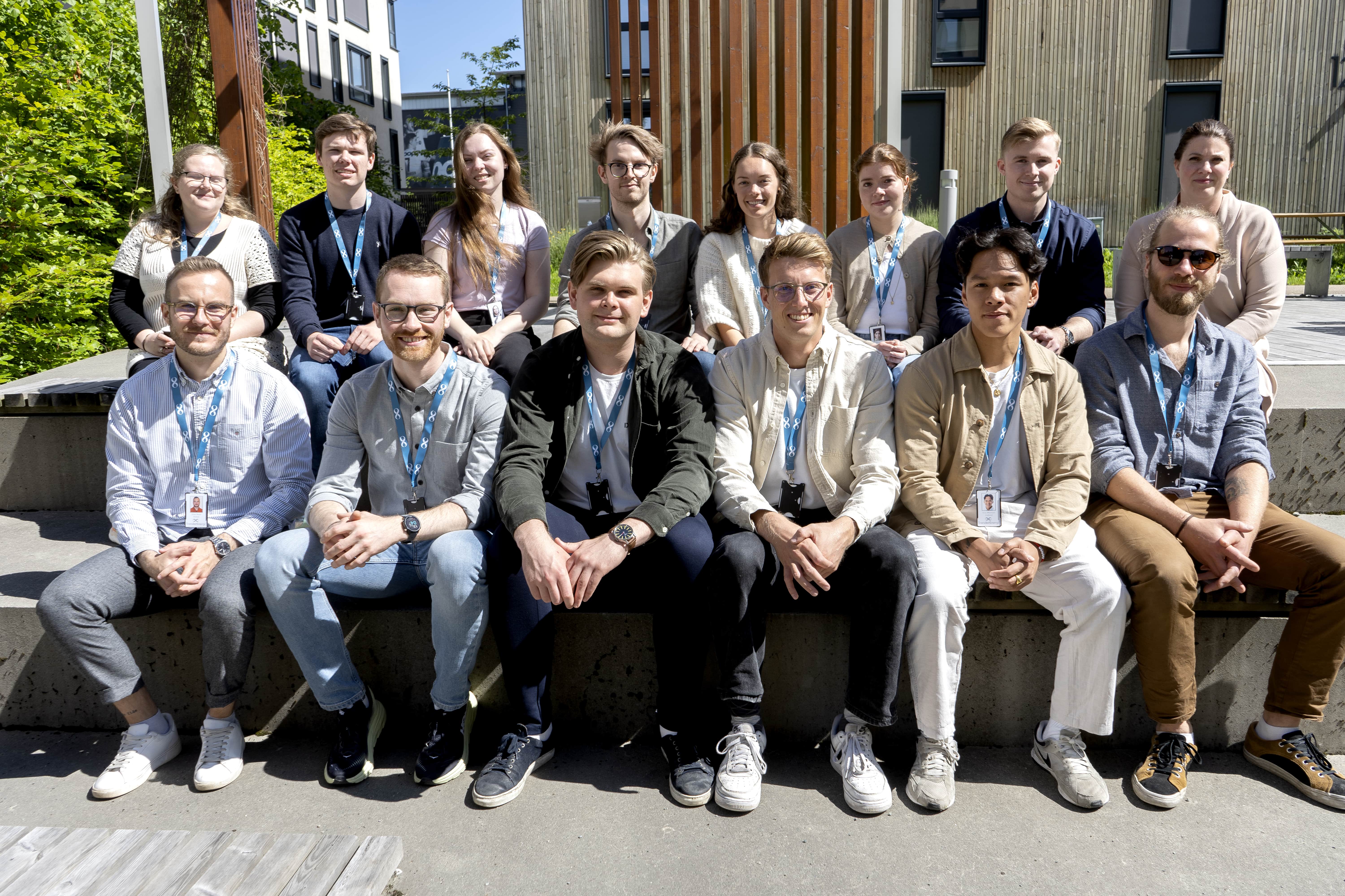 Group photo of many smiling students sitting on steps with lanyards around their necks, collaborating with Aneo