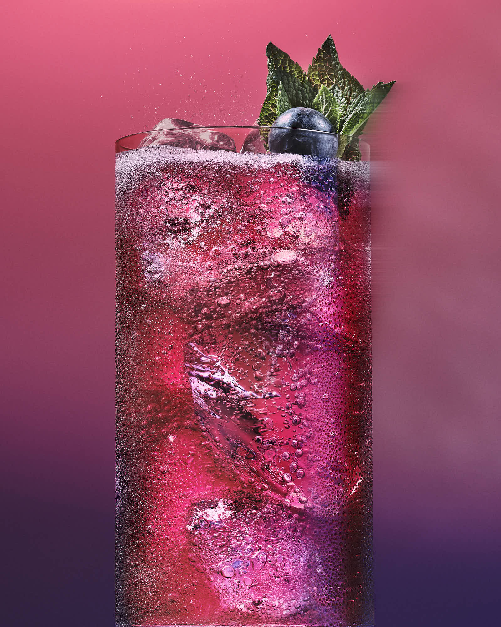 A vibrant pink cocktail garnished with mint, served in a tall glass against a colorful gradient background.