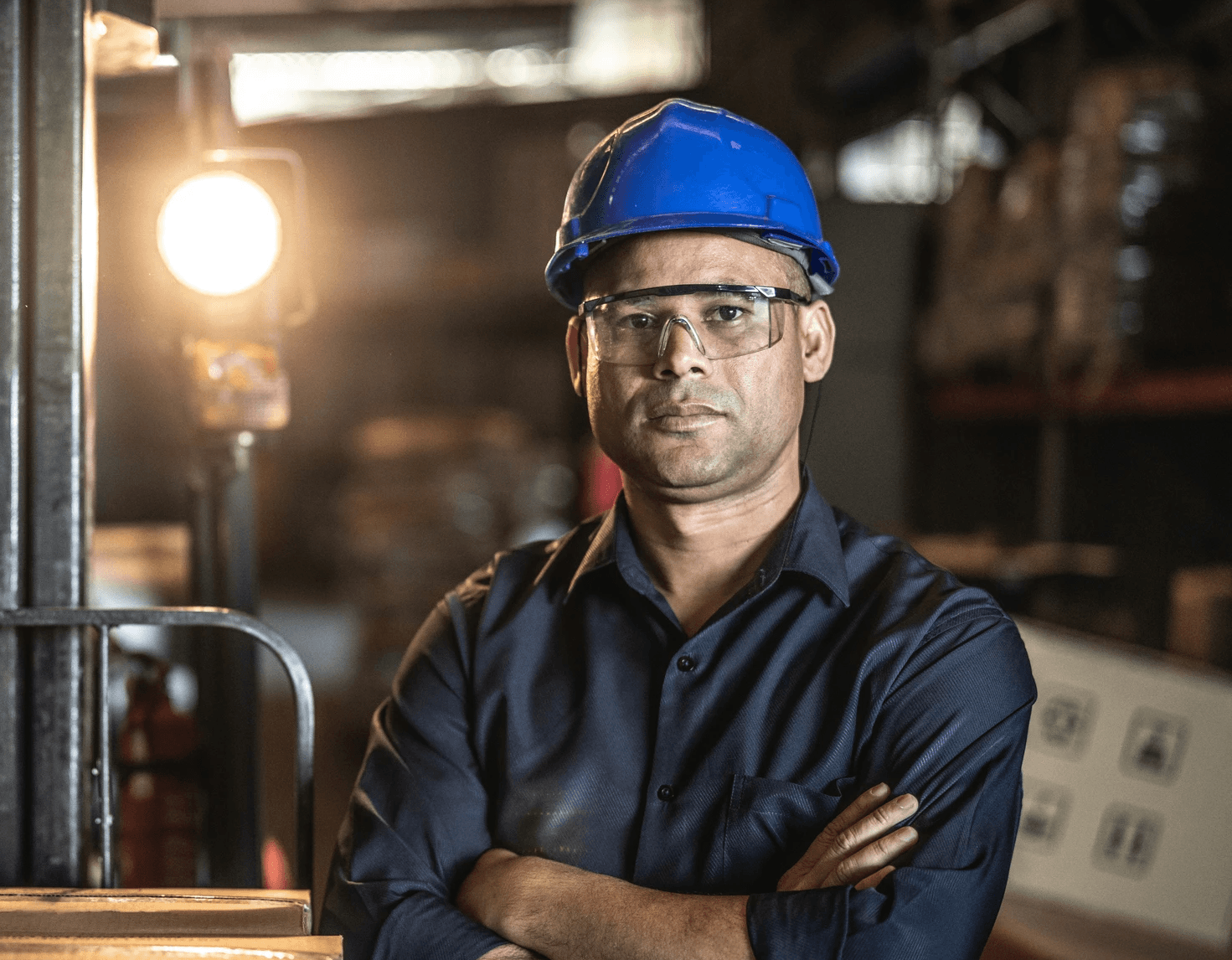 photo of a man in a blue hard hat standing in a factory and staring at the camera