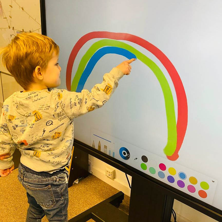 A younger child is using a digital whiteboard to draw a rainbow using a crayon effect.