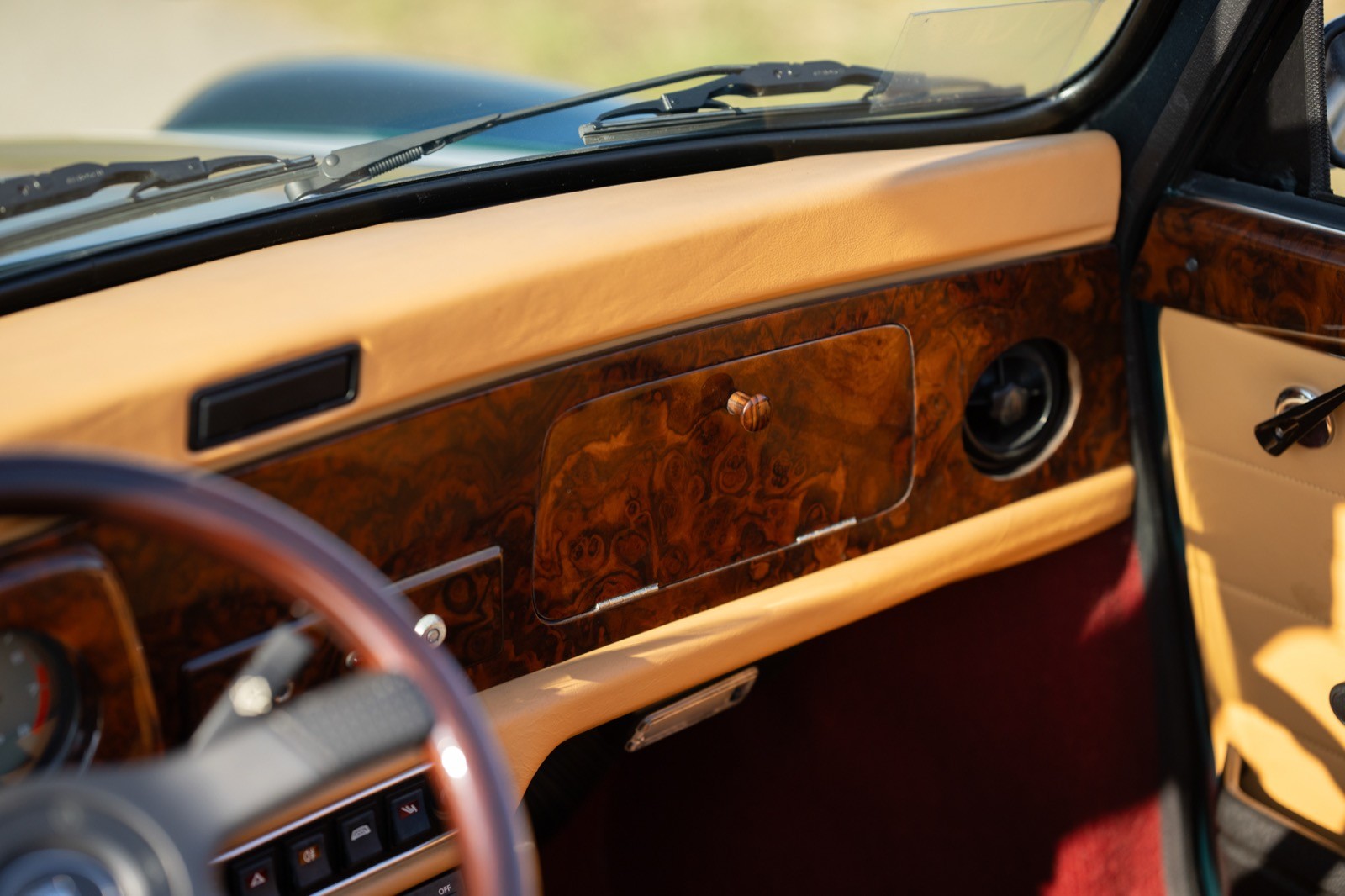 A close-up view of a car's wooden dashboard, featuring dials and controls with a leather-wrapped steering wheel.
