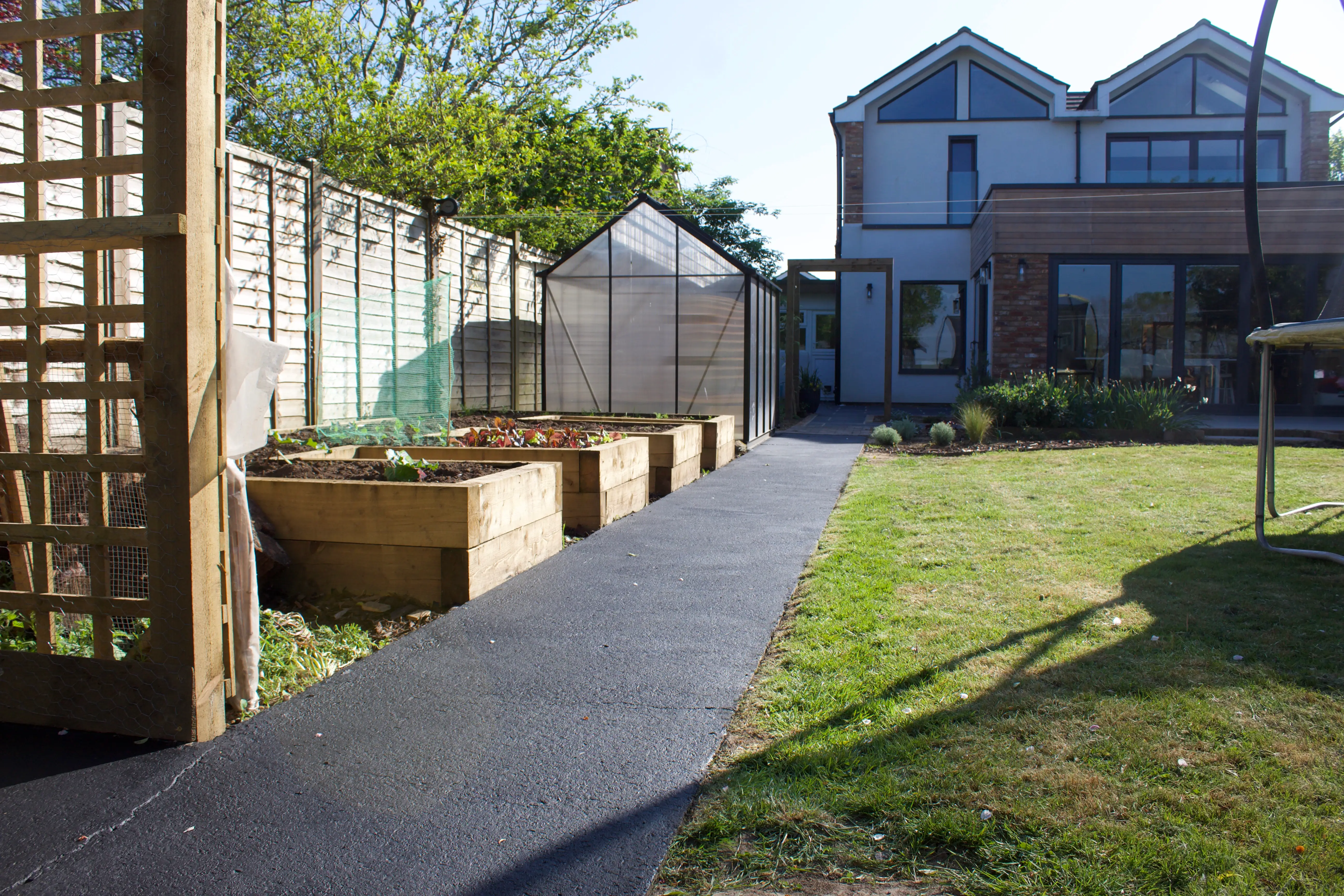 A pathway leads through a garden with wooden planters and houses in the background under clear blue skies.