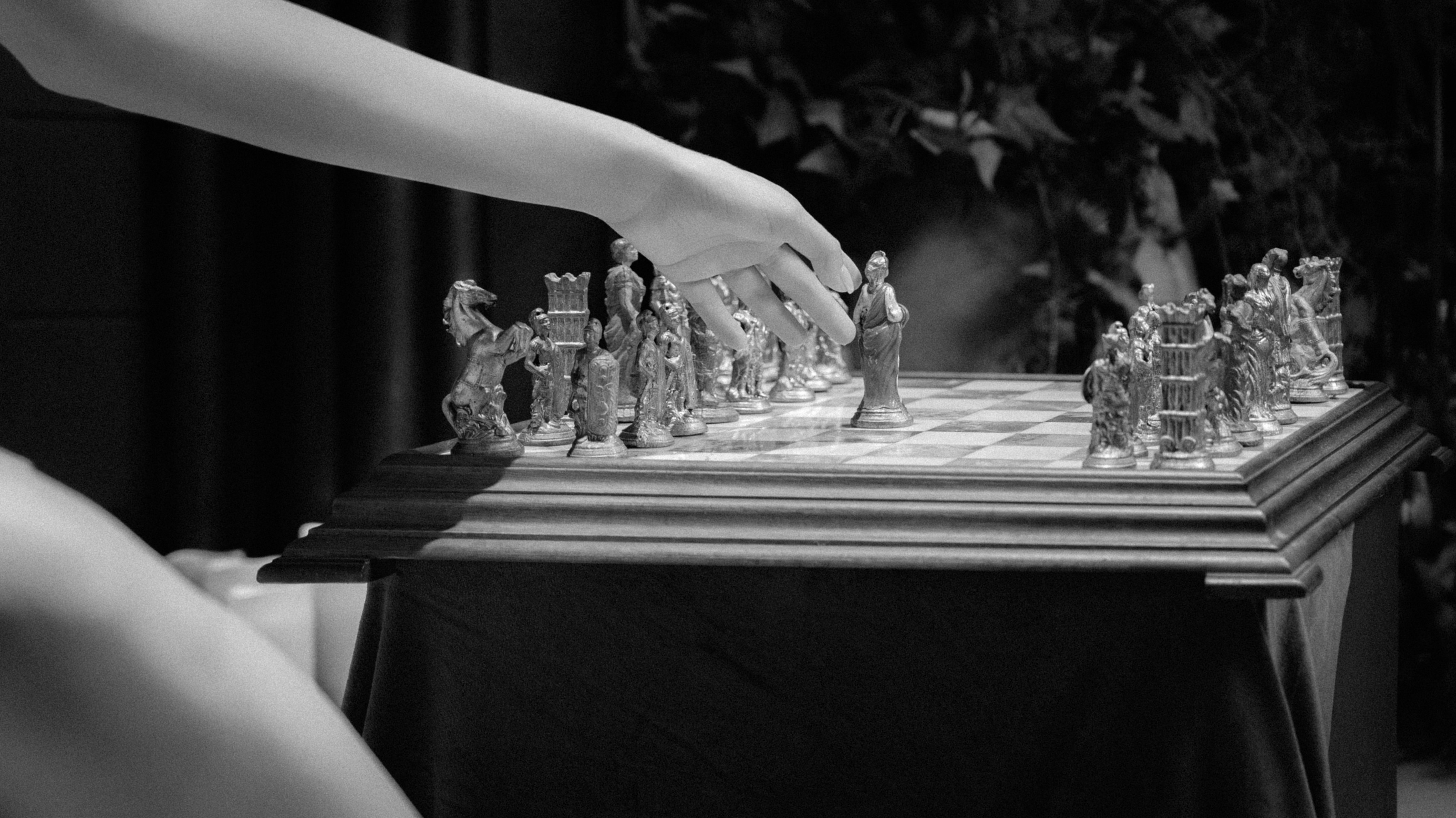 Detaliu alb-negru cu o mâna mirei mutând piese de șah, fotografie artistică editorială într-un decor elegant de nuntă în București