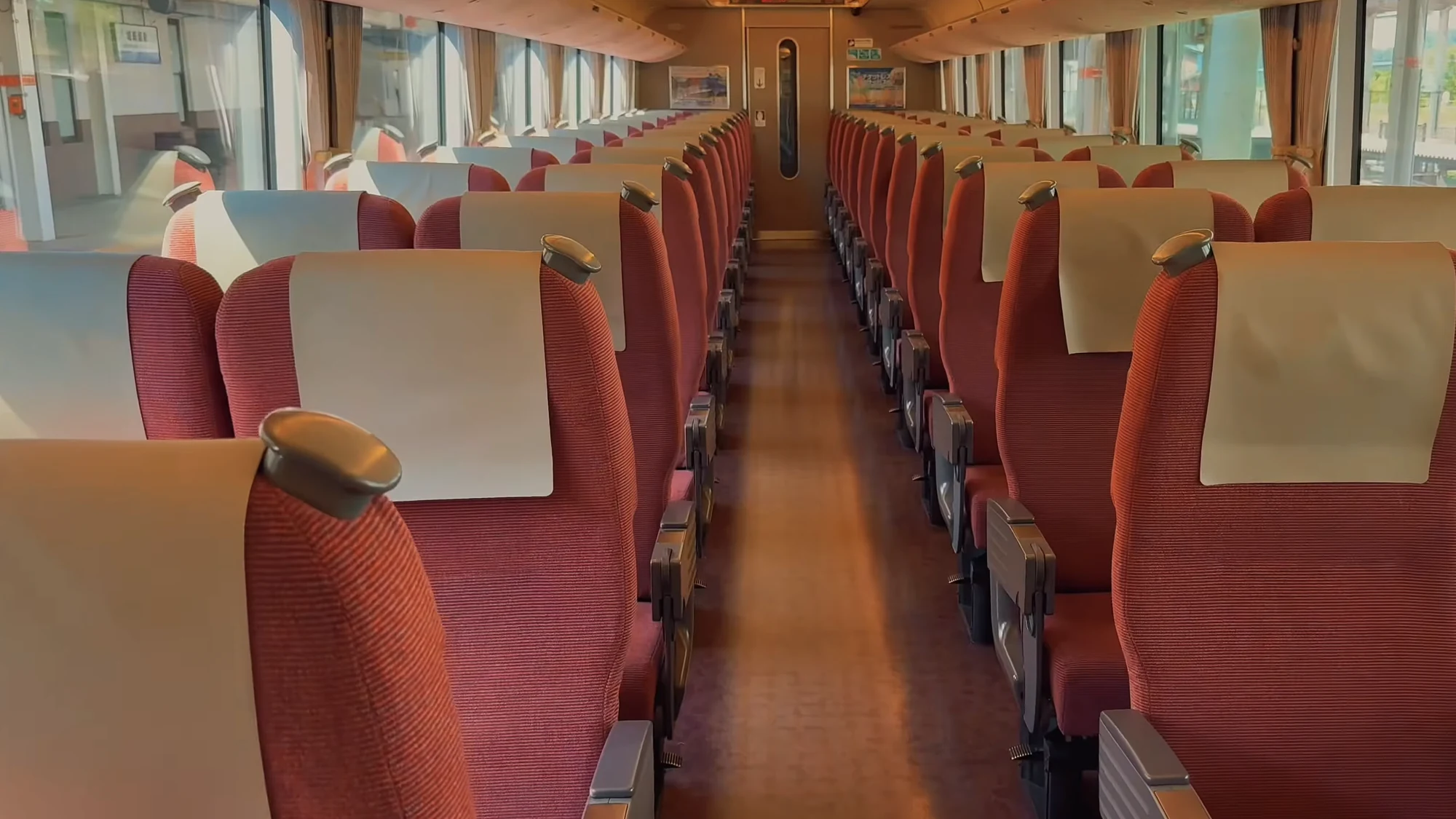 The empty interior of a limited express carriage with rows of red reclining seats.