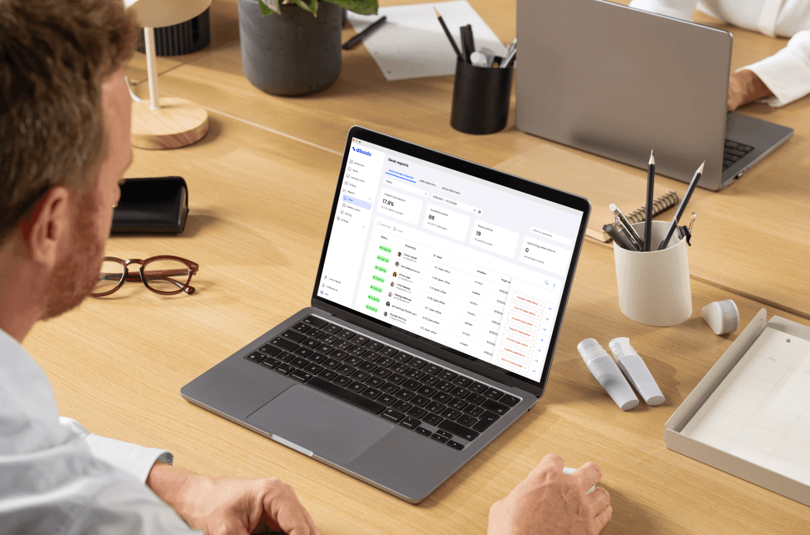 Workplace operations lead reviewing an attendance and utilization dashboard on a laptop, with an open-plan office visible in the background