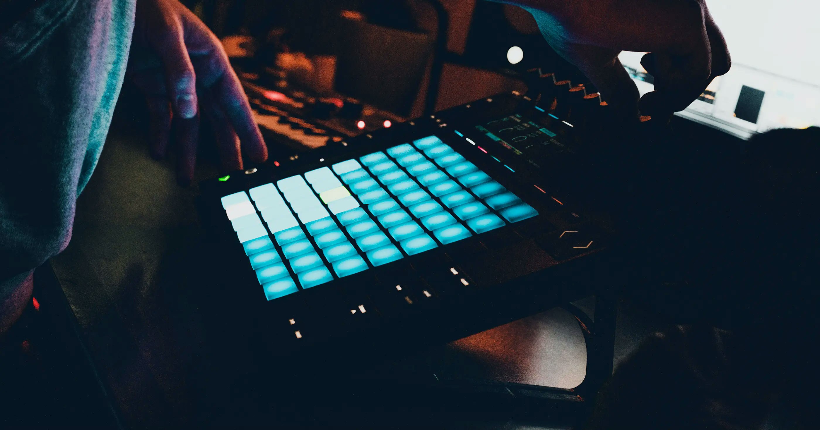 Music producer using an Abelton Push MIDI controller in a dimly lit studio.