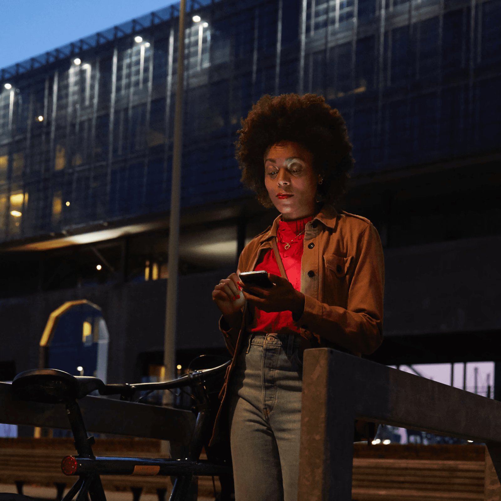 Een vrouw die in de avond op straat naar haar mobiele scherm kijkt. 