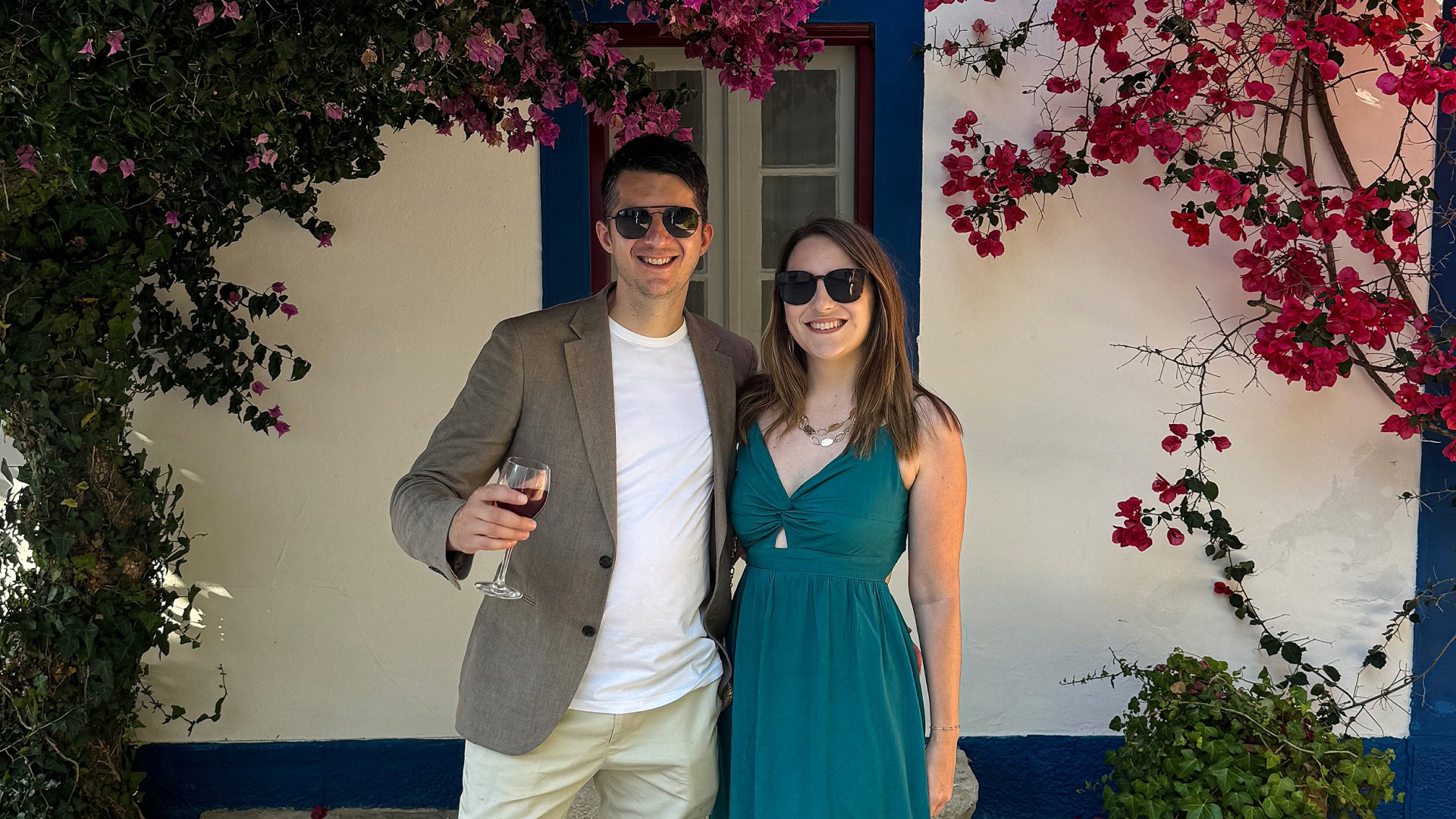 A bride and groom hold hands tenderly, the bride's bouquet of dried flowers hanging low. They stand in a softly lit, elegant interior, conveying romance.