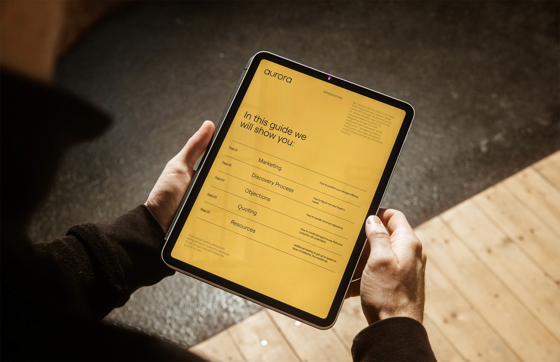 A person holds a tablet displaying a yellow "Introduction" guide titled "In this guide we will show you: Marketing, Discovery Process, Objections, Quoting, Resources." This illustrates a specialized B2B sales tool UI, designed to streamline the solar project lifecycle and customer education.