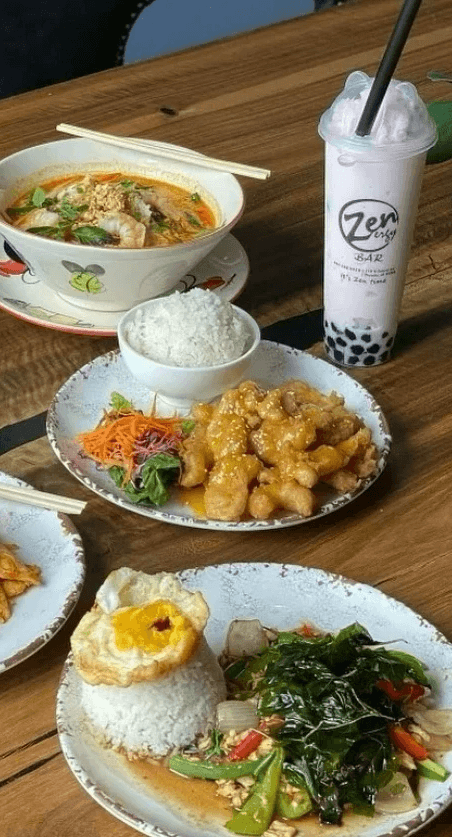 Three full plates of delicious thai food and a boba drink on a dinner table