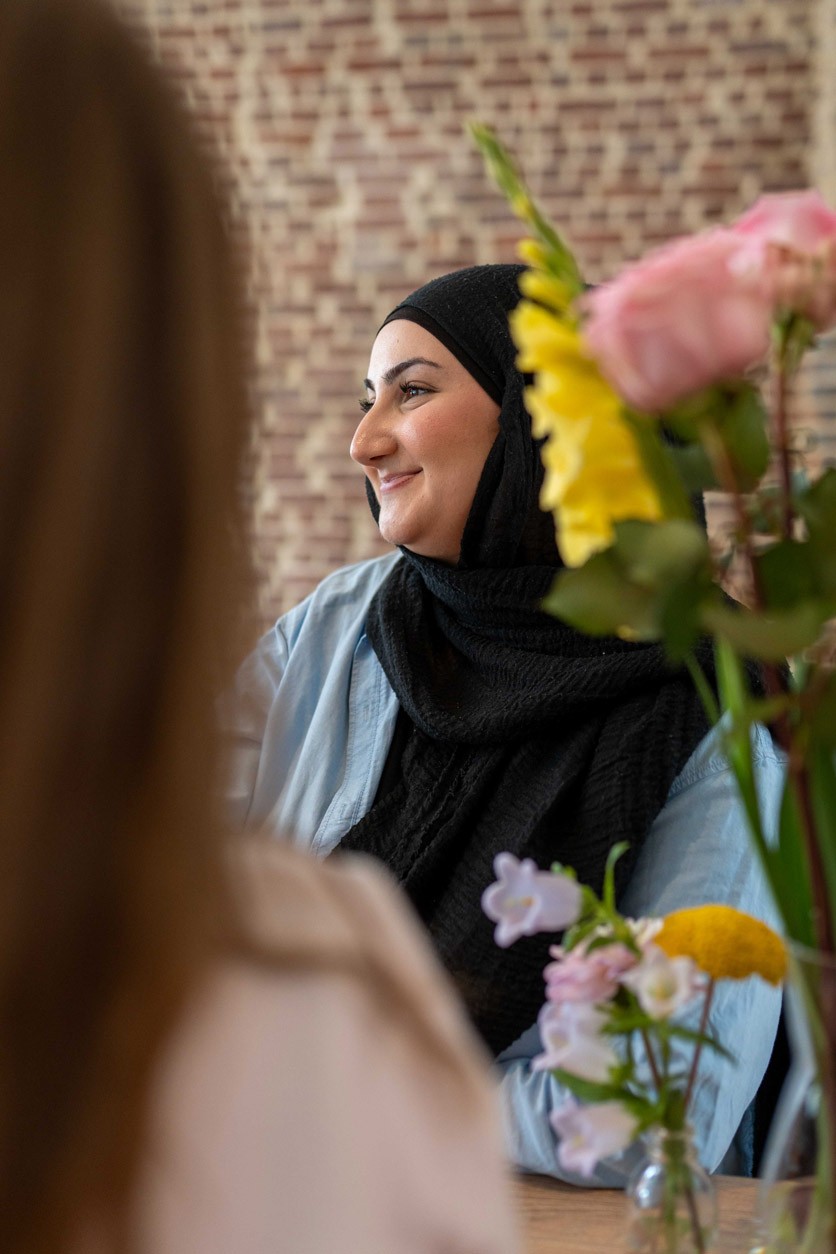 Mitarbeiterin mit Kopftuch sitzt im Gespräch in einem modernen Besprechungsraum von SLB, im Vordergrund Blumen.
