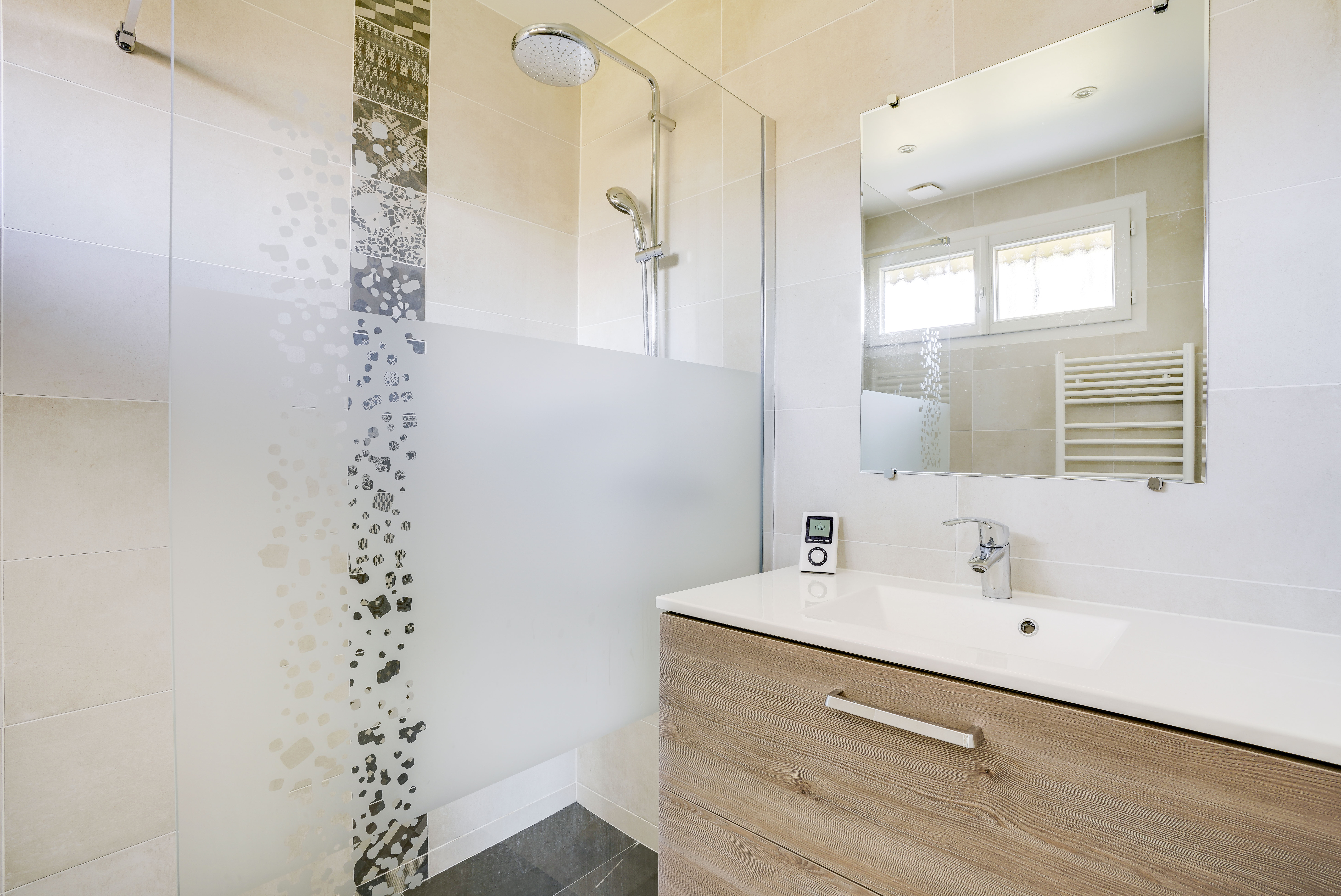 Rénovation salle de bains Paris Est avec douche verre dépoli, carrelage décoratif et meuble-lavabo bois, fenêtre lumière naturelle, architecte d'intérieur.