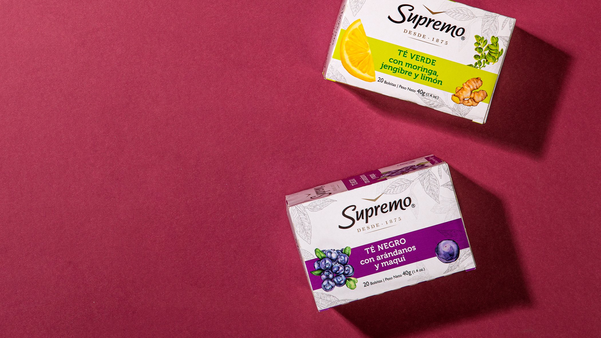 Two Supremo tea boxes on a burgundy background. The top box is green tea with ginger and lemon; the bottom is black tea with blueberries and maqui.