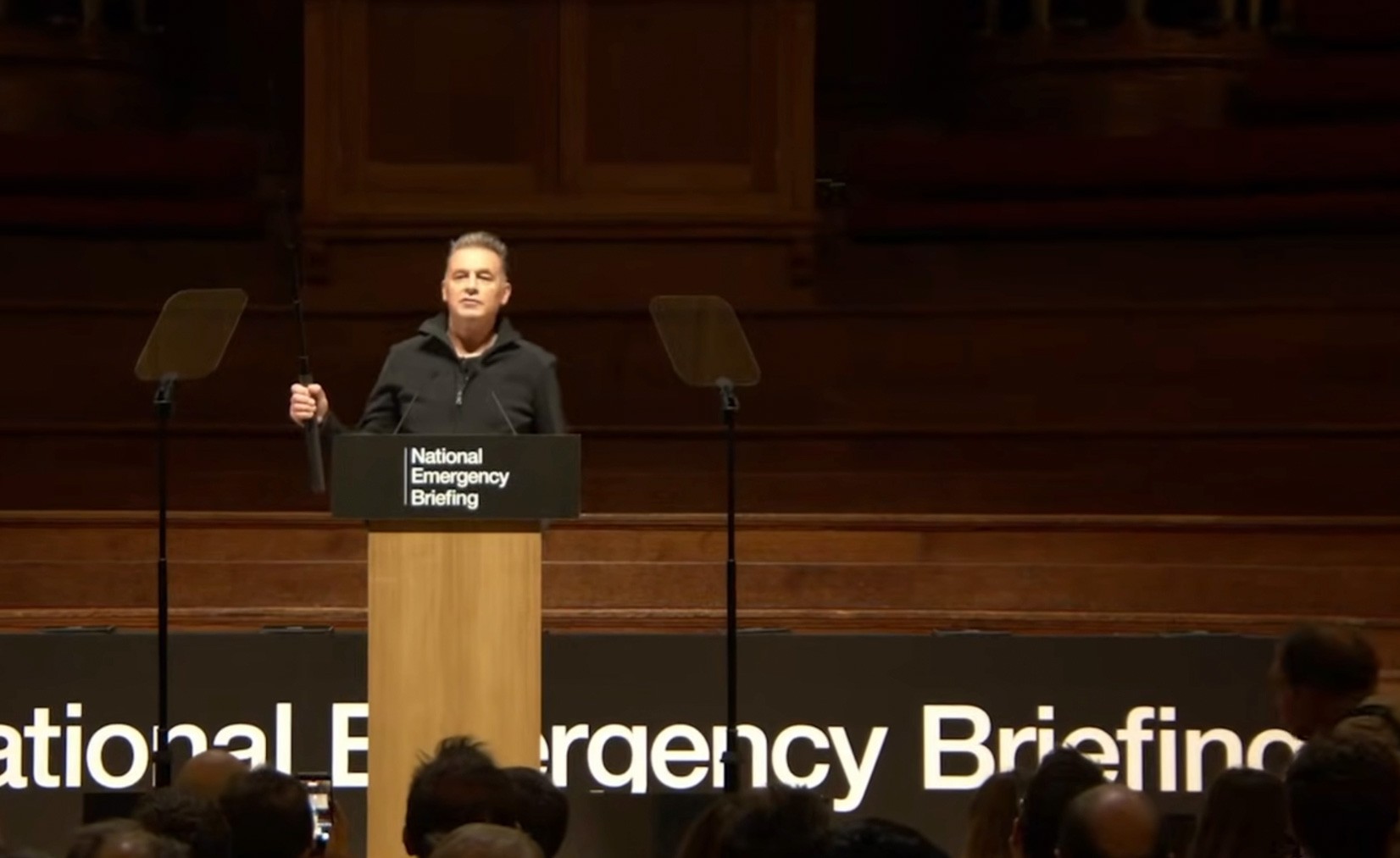 Chris Packham holding selfie stick at podium during National Emergency Briefing on climate and nature crisis
