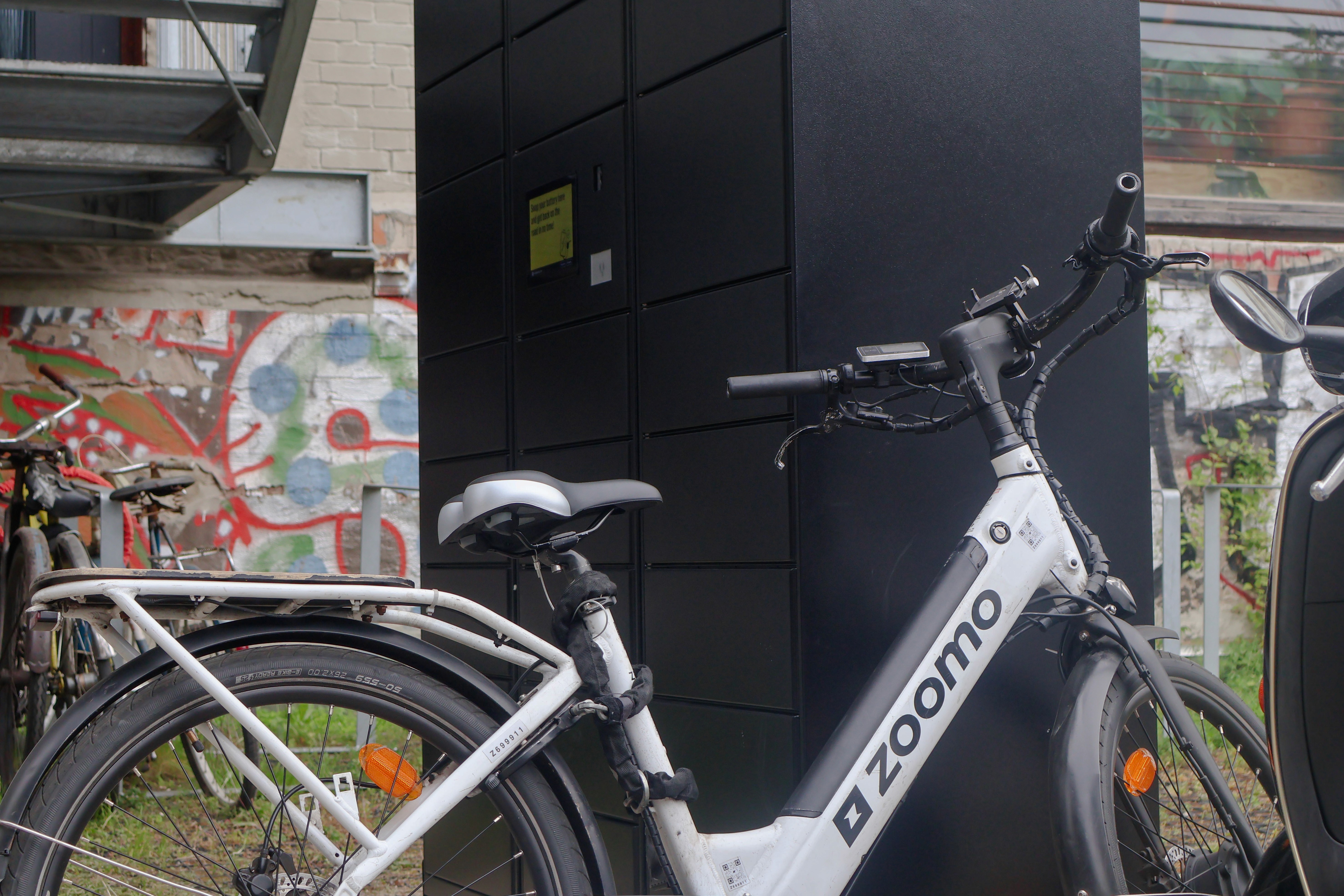 A Zoomo delivery e-bike parked beside a PowerShelter SmartSwapping locker at Impact Hub Berlin, one of the network's early locations.