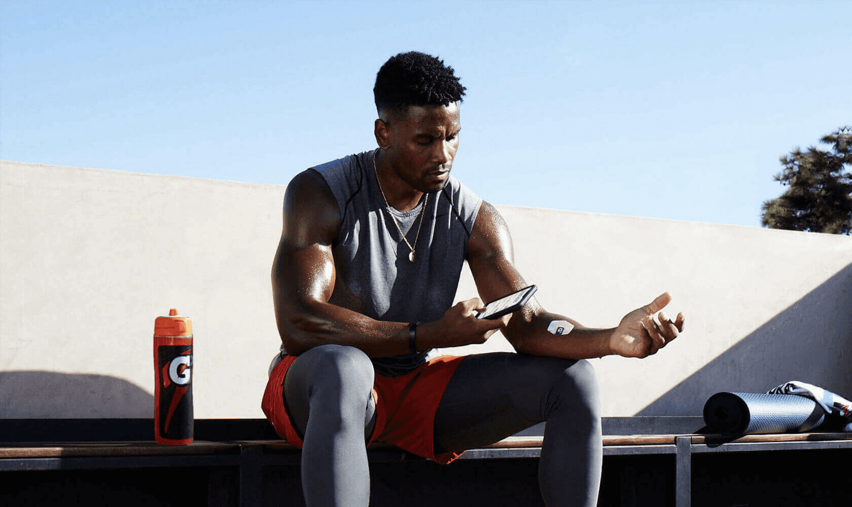 Black man sitting down on park bench using his phone to scan his Gatorade sweat patch.