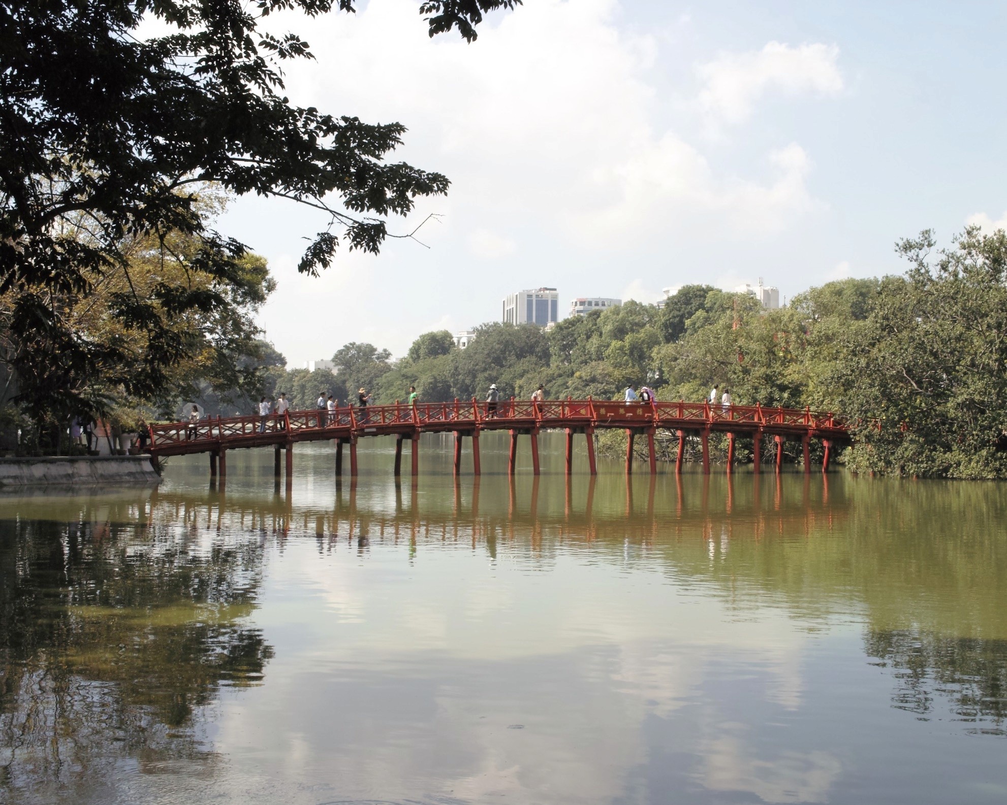 Photo du pont rouge du lac de la vielle ville de Hanoi pris de face avec plusieurs passants dessus qui se dirigent vers un temple qui se situe sur une petite île au milieu du lac