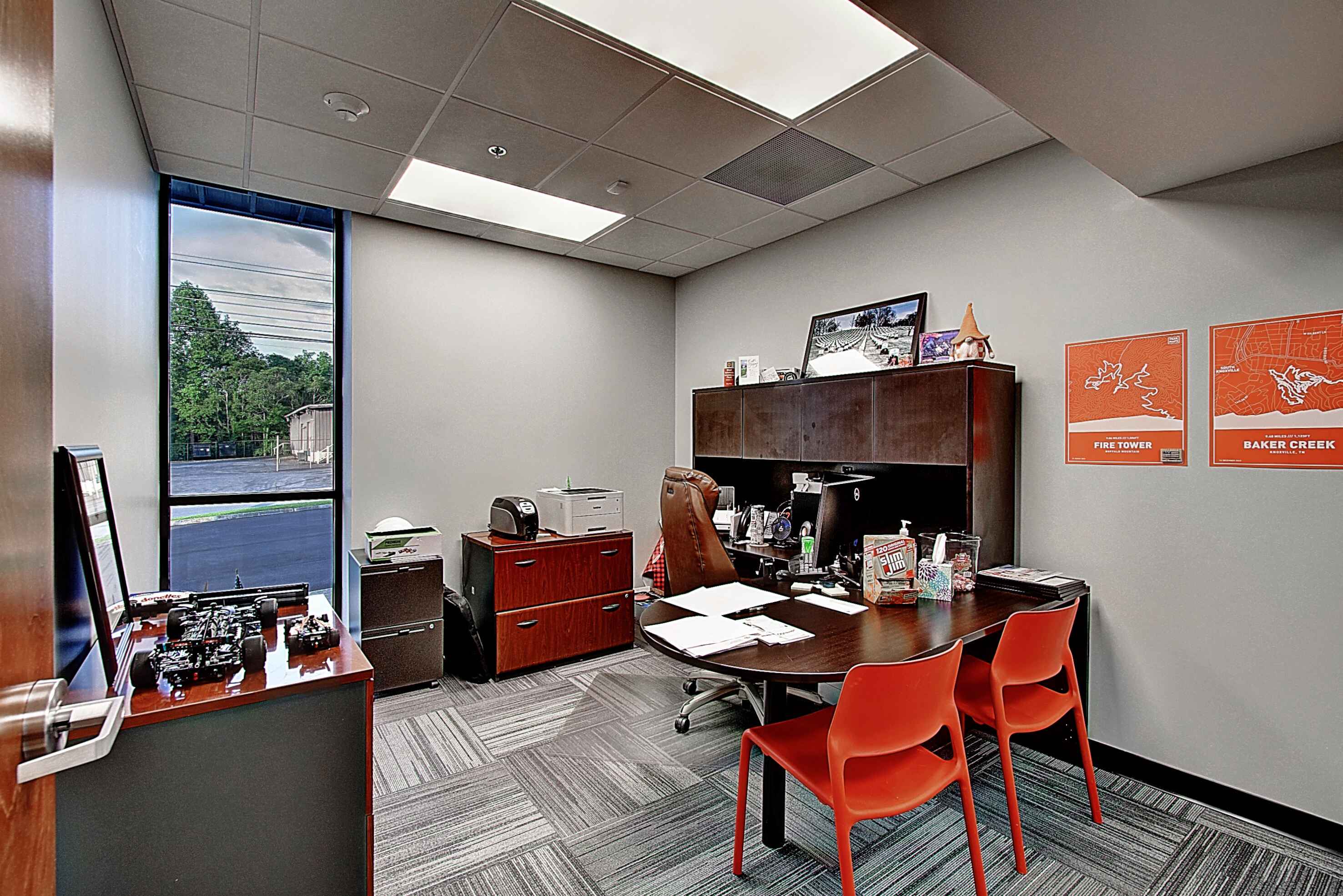 An office space featuring a desk, orange chairs, and a scenic wall mural in a bright, modern environment.
