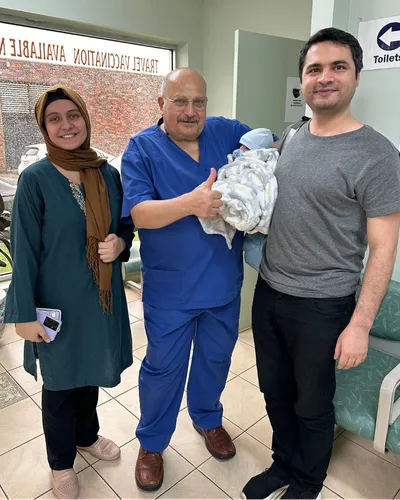 Dr. Ashraf Saddik giving a thumbs up alongside a mother and father holding their newborn baby at the Coburg clinic.