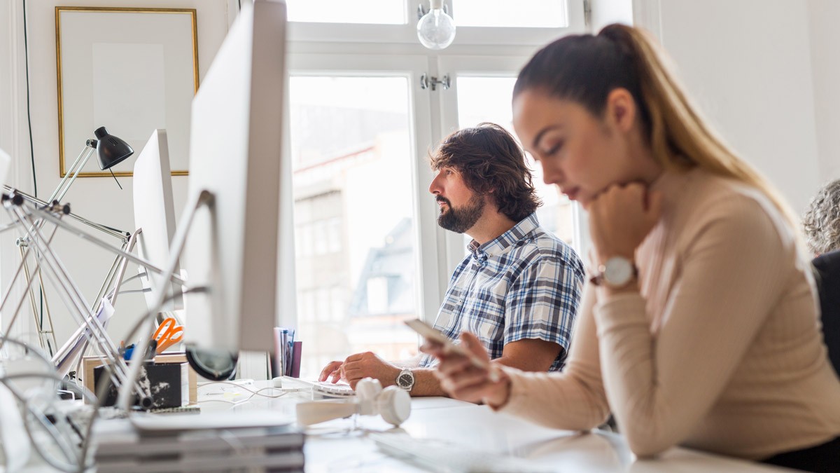 Two collegues sitting side by side at their desk while working on their computers