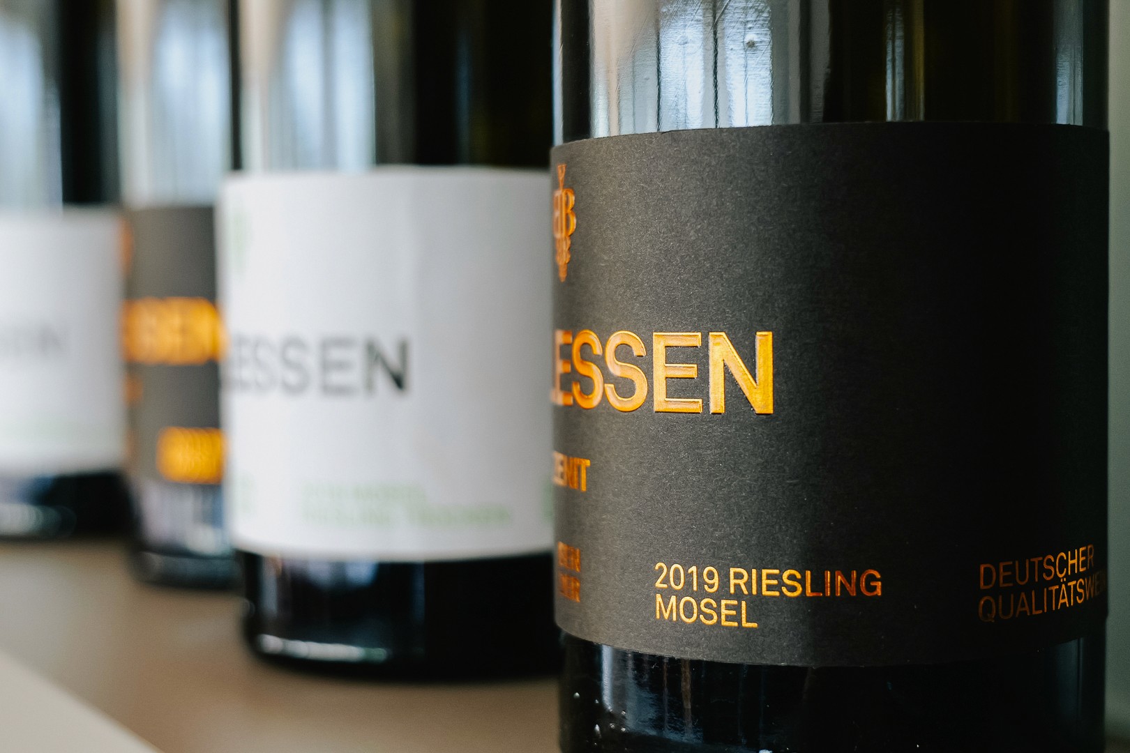 A close-up of wine bottles with different colored labels, standing in a row on a countertop.