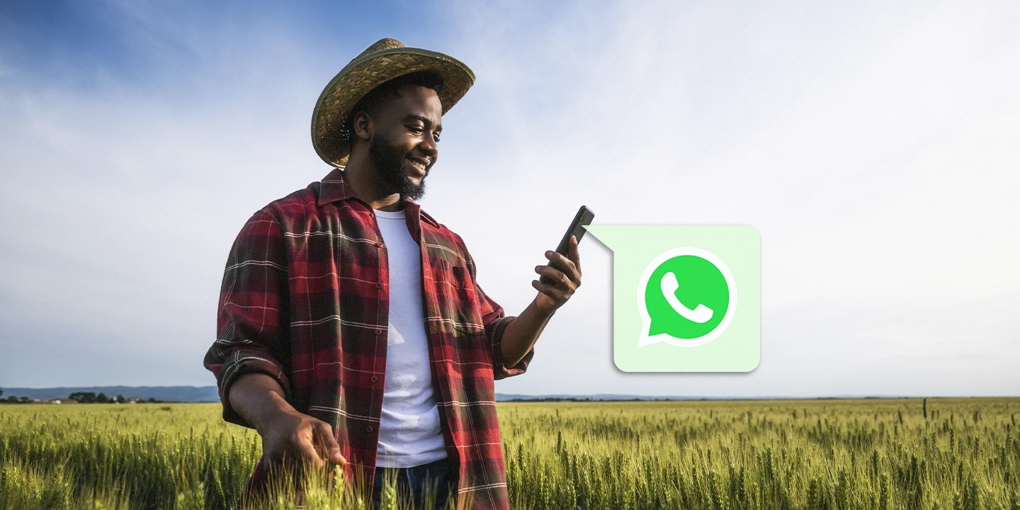 Homem sorridente com chapéu de palha e camisa xadrez segurando um celular em um campo de trigo, representando o uso do WhatsApp para comunicação no setor agro