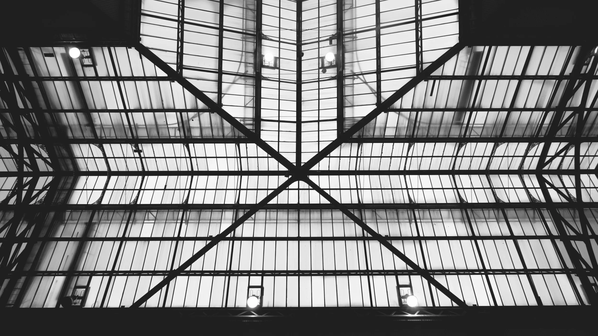 Geometric patterns of light and shadows created by a large glass structure, viewed from below.
