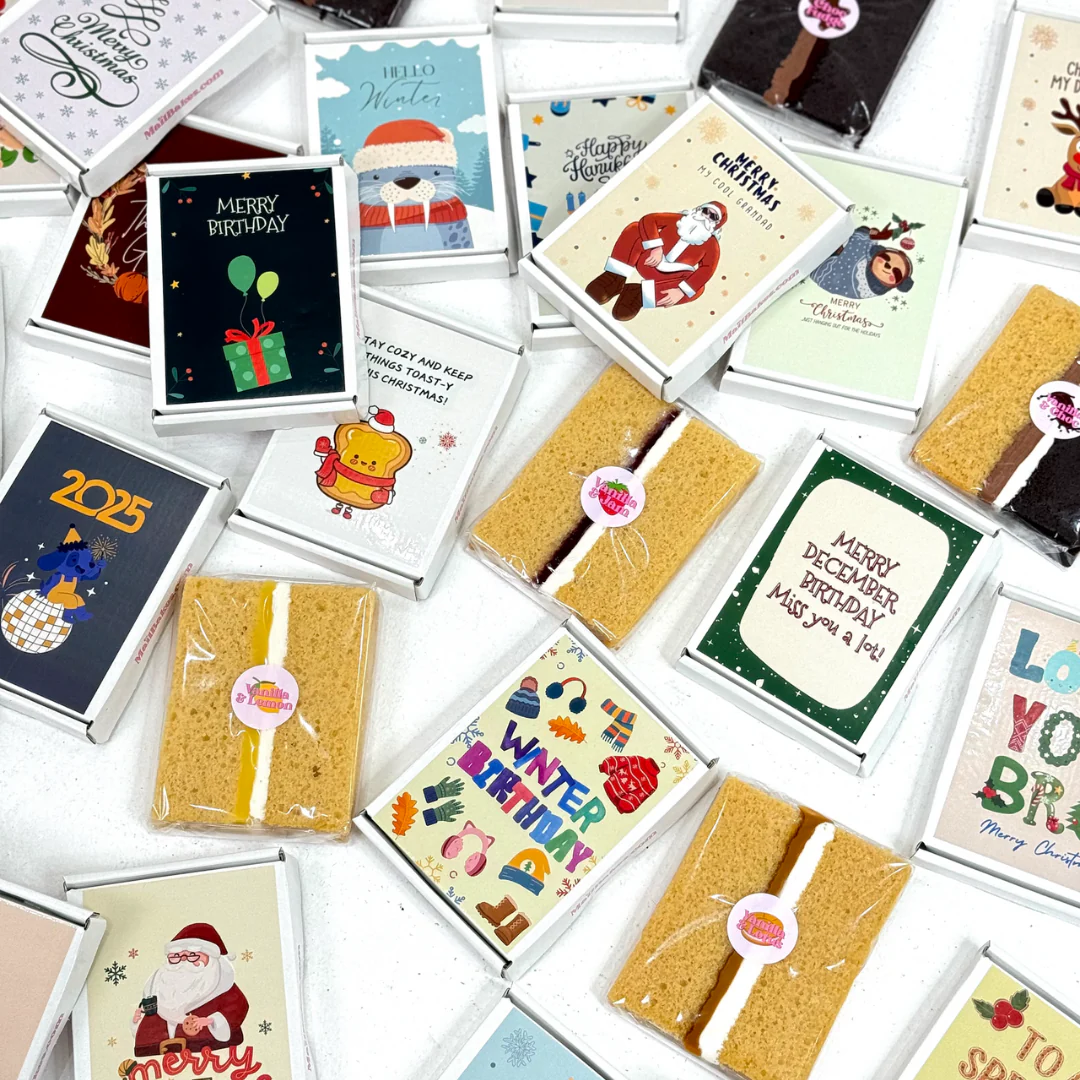 A collection of holiday-themed matchbox-style boxes with various festive designs including Santa Claus, winter scenes, and holiday greetings. Some boxes contain what appears to be cake slices with cream filling.