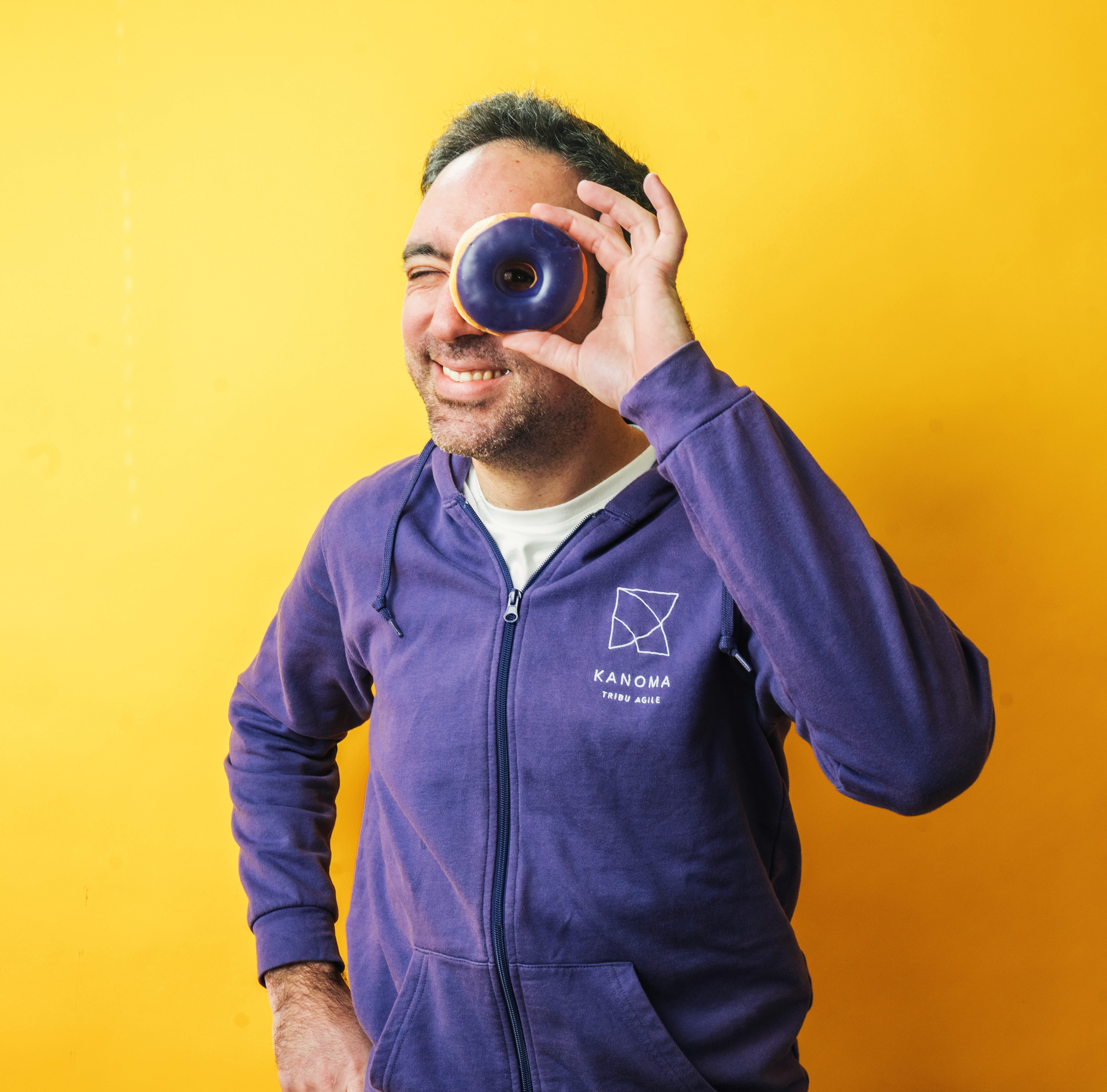 un homme qui porte un sweat violet et regarde à travers le trou d'un donut