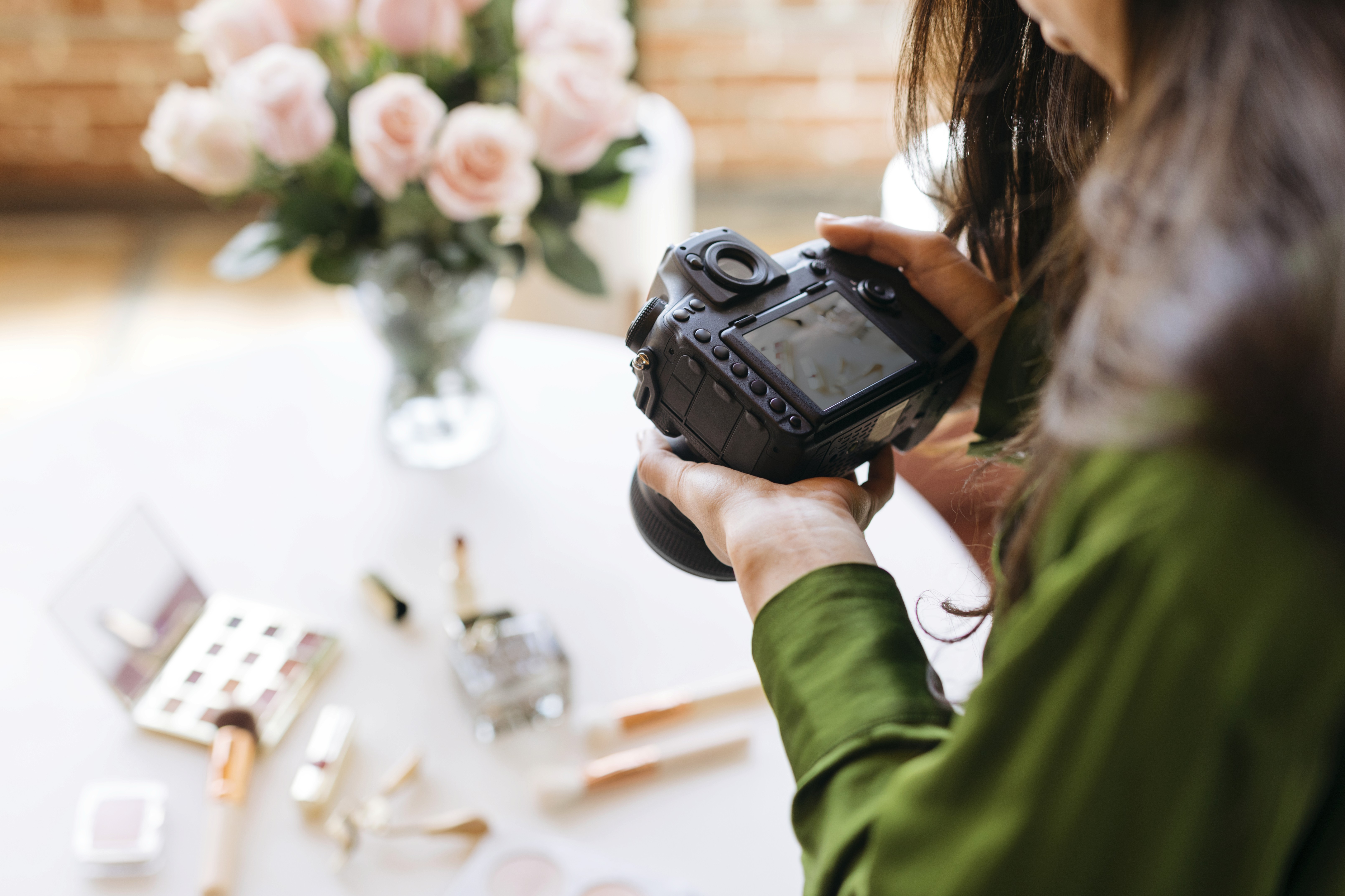 Female photographer reviewing photos on camera with roses and wedding details