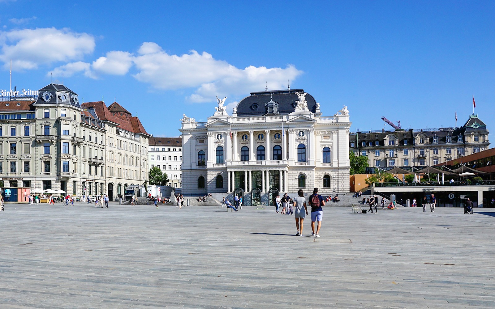 Operahuset i Zürich med människor som promenerar på Sechseläutenplatz en solig dag.