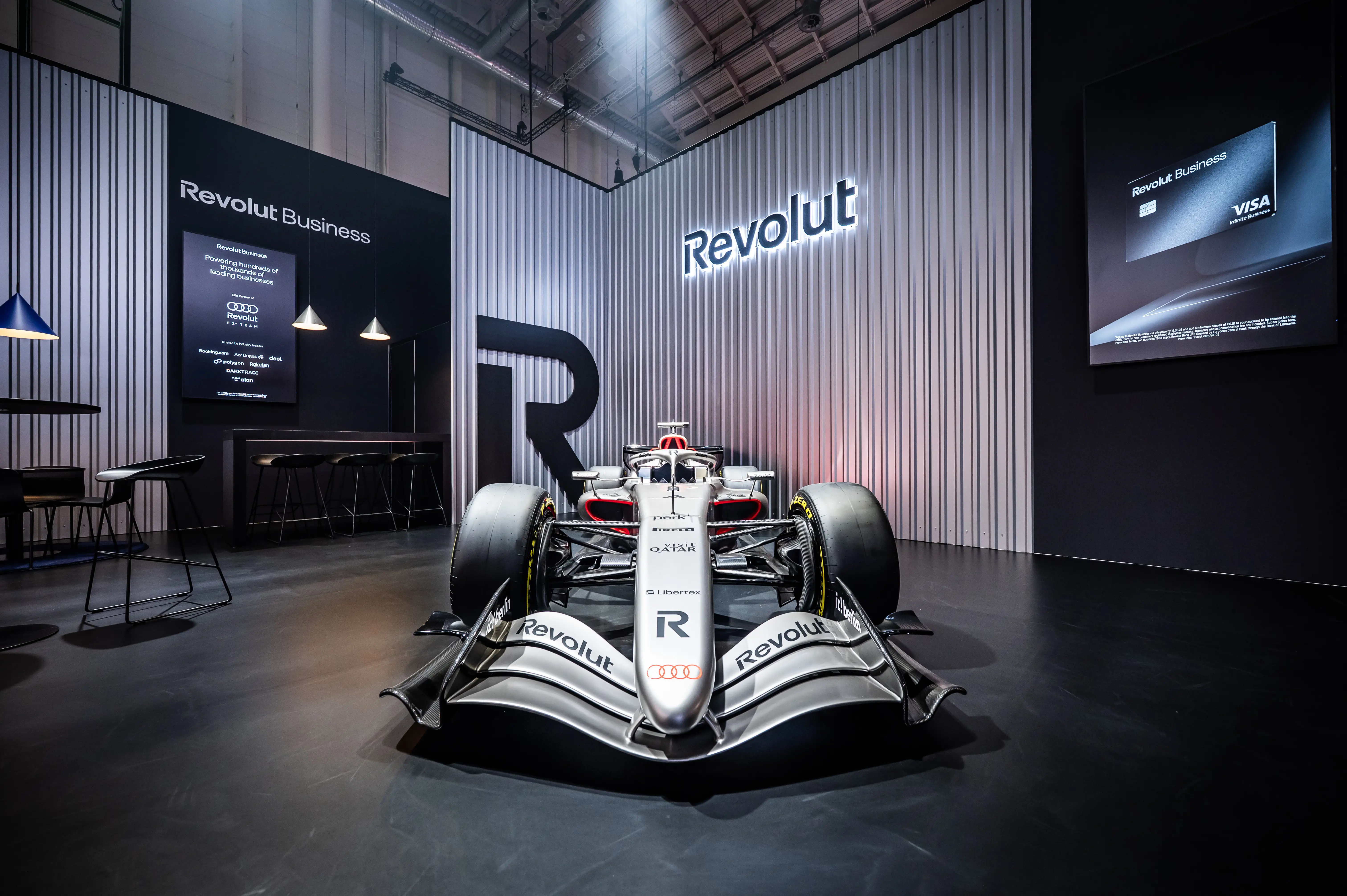 Front view of the Revolut booth with Formula 1 car, glowing logo and silver corrugated walls.