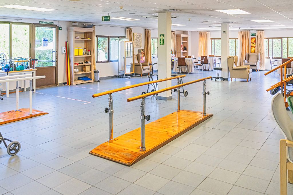 Spacious rehabilitation area with wooden parallel bars and a lounge seating area in the background.