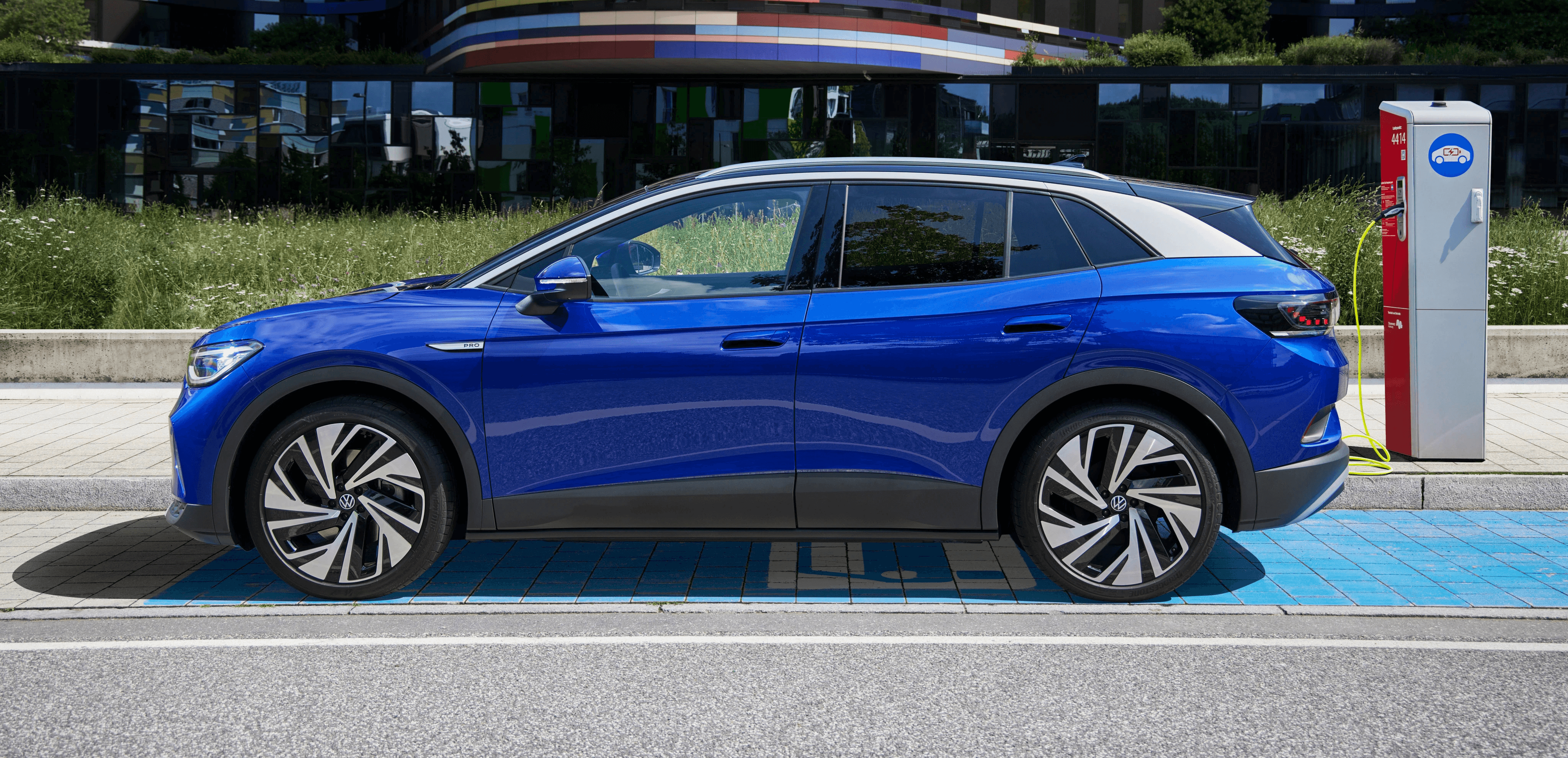 Volkswagen ID.5 bleue branchée à une borne de recharge en ville, SUV coupé électrique vu de profil