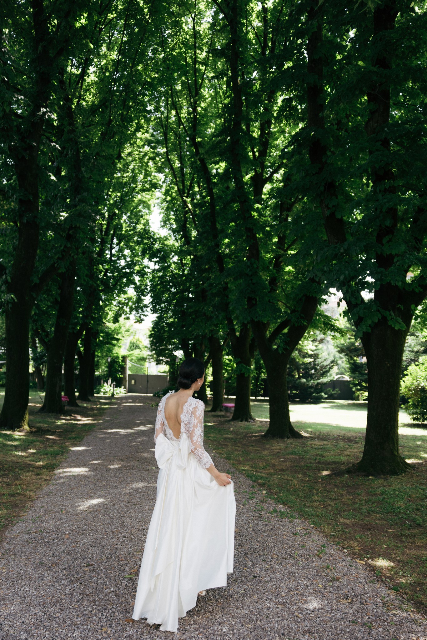 Sposa in abito bianco cammina sotto il viale di alberi, luce naturale tra le fronde, reportage matrimoniale a Villa Privata