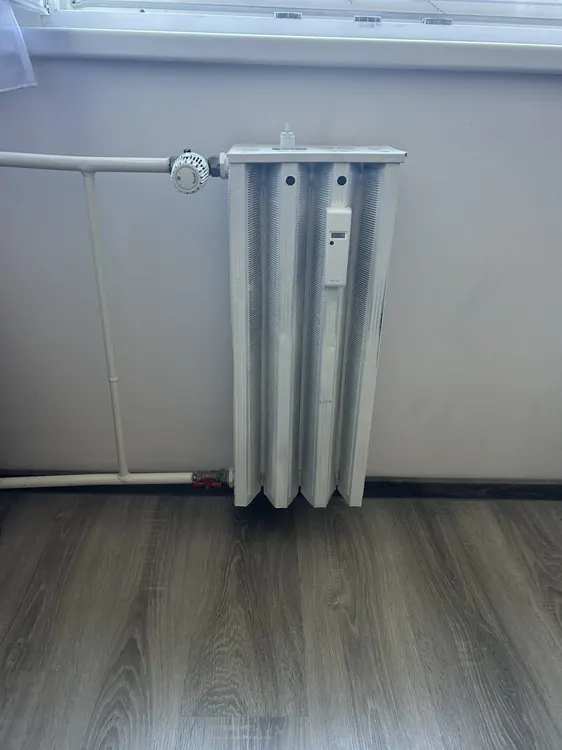 Fűtési csövekkel bekötött radiátor szürke laminált padló felett