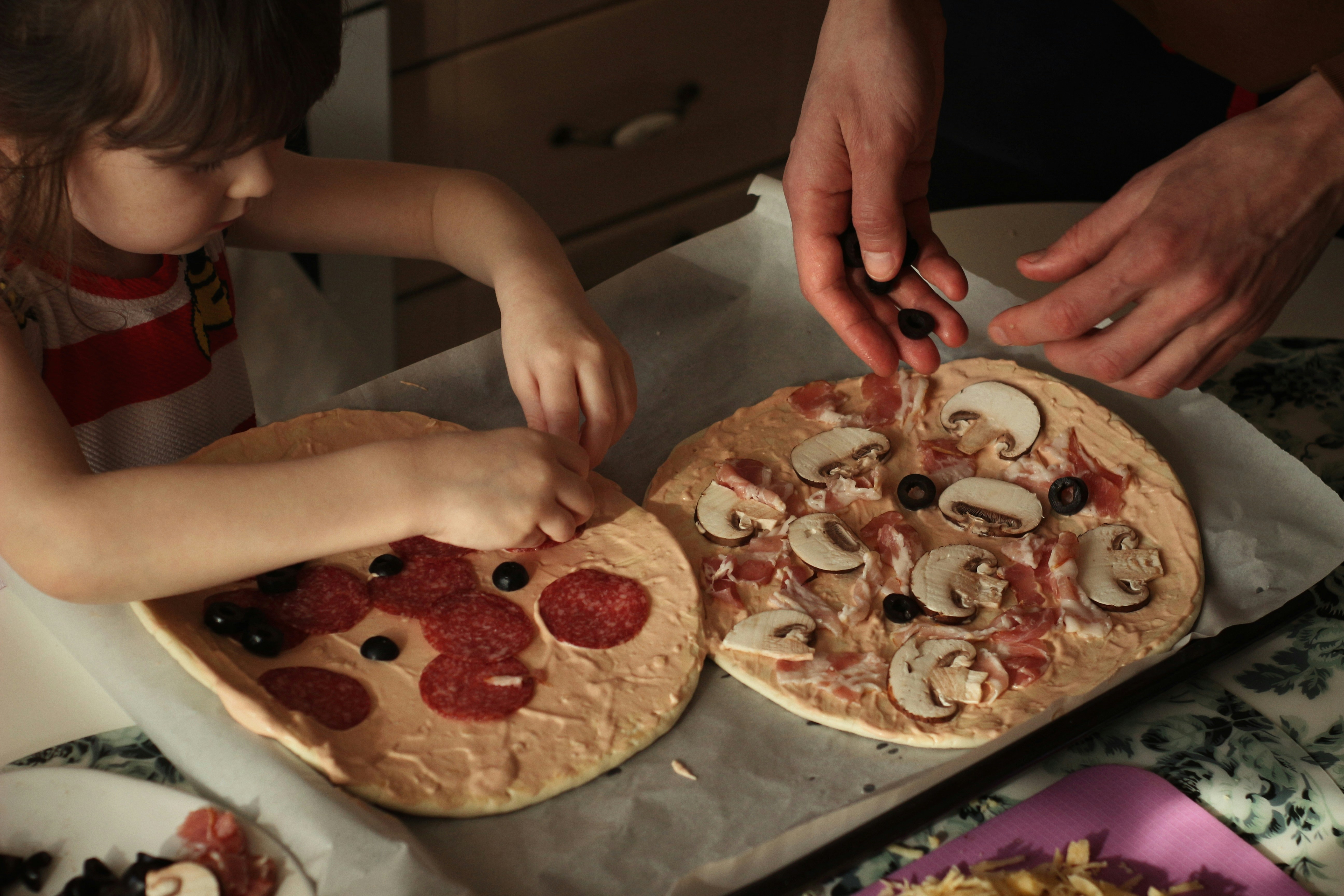 Children topping homemade pizzas with mushrooms and pepperoni