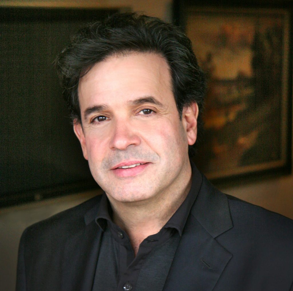 white man with dark hair and a dark shirt and suit jacket looking at camera