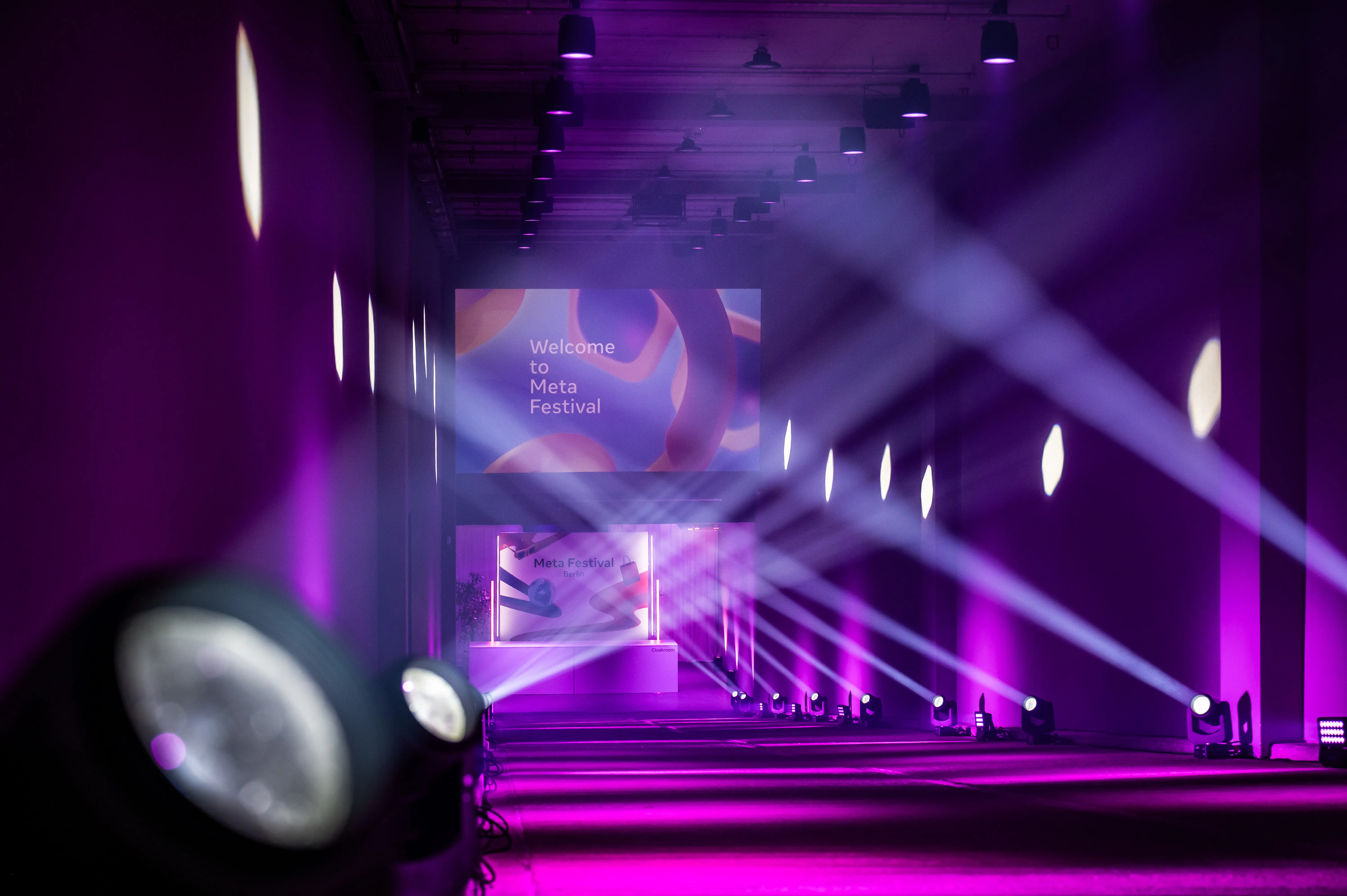 Purple corridor with moving head spotlights and Welcome to Meta Festival projection.