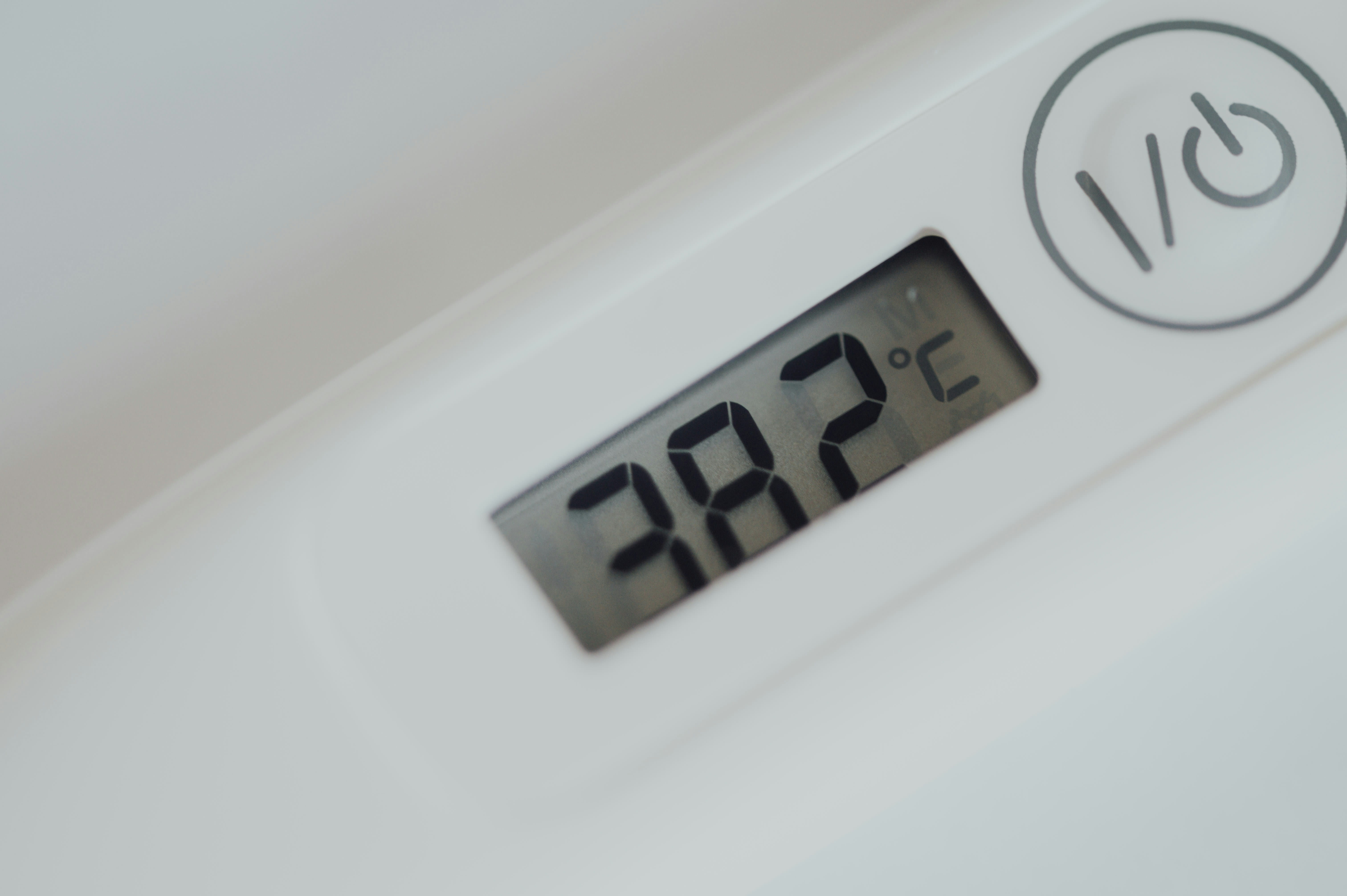 Close-up of an electronic thermometer showing a temperature of 38.2°C. The device has a white body with a power button symbol nearby.