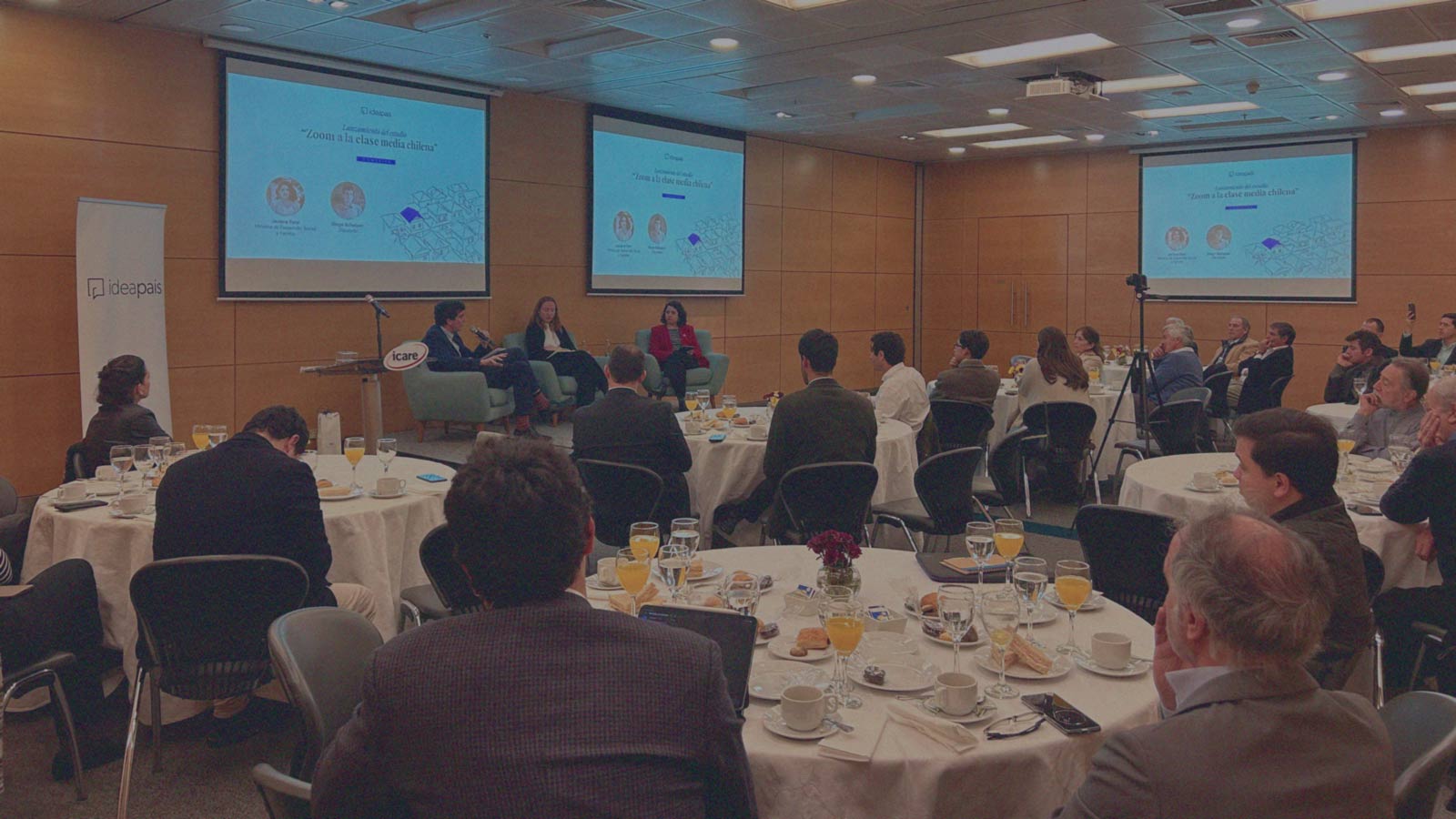 Profesionales jóvenes observan una exposición, sentados alrededor de mesas, en una actividad de IdeaPaís.