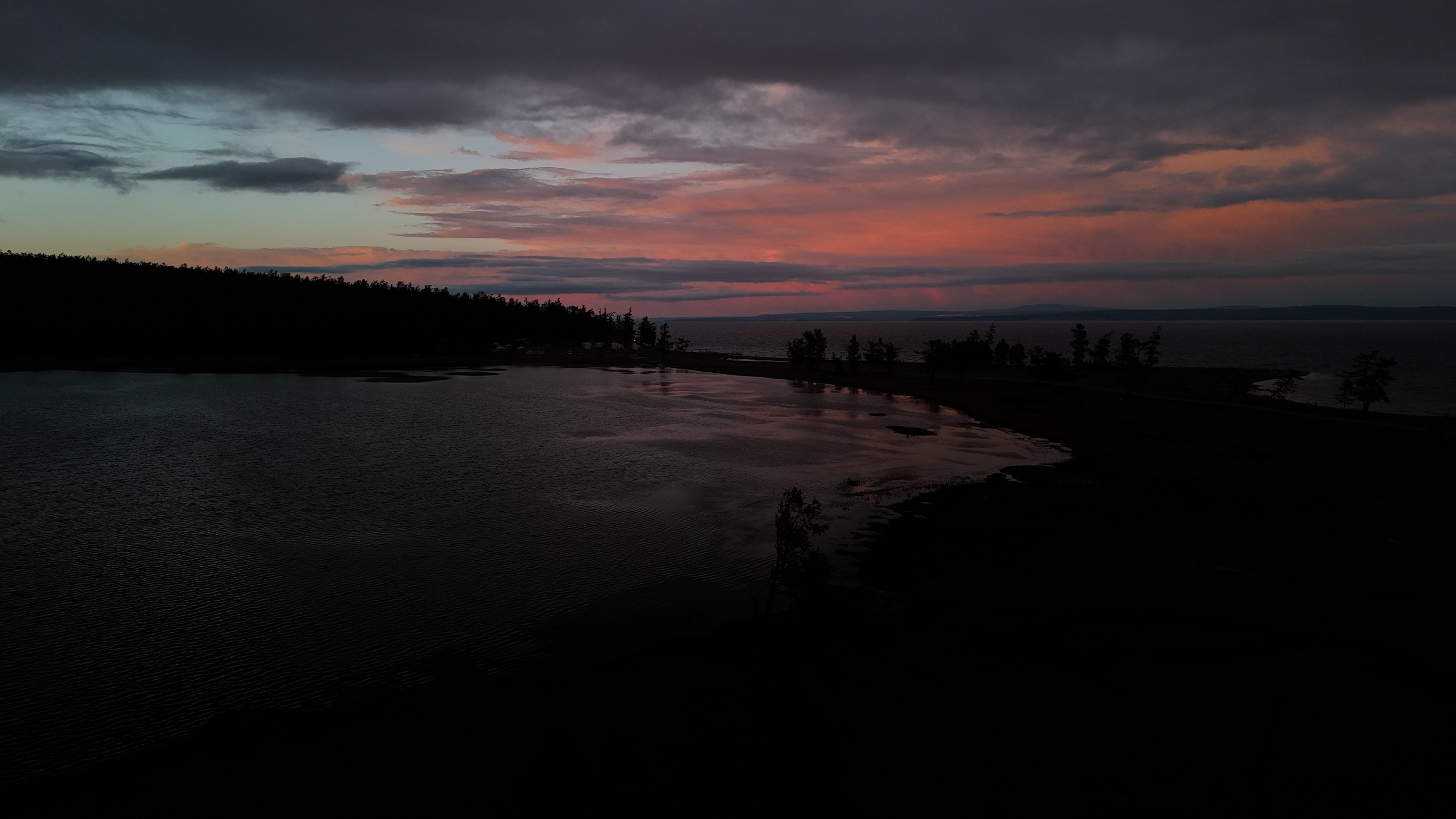 A smiling young man with crossed arms, wearing a plaid shirt and white t-shirt, poses against a dark background.