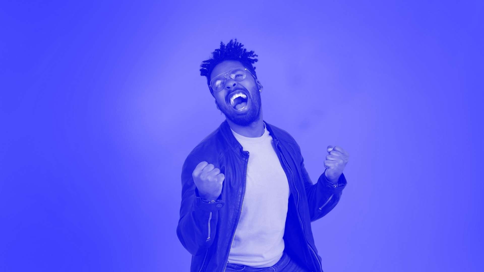 A man wearing glasses with his fist in the air celebrating